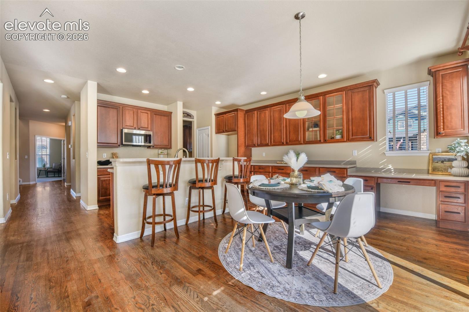 Wood-finish flooring throughout, kitchen with wood cabinetry, stainless steel microwave, and recessed lighting