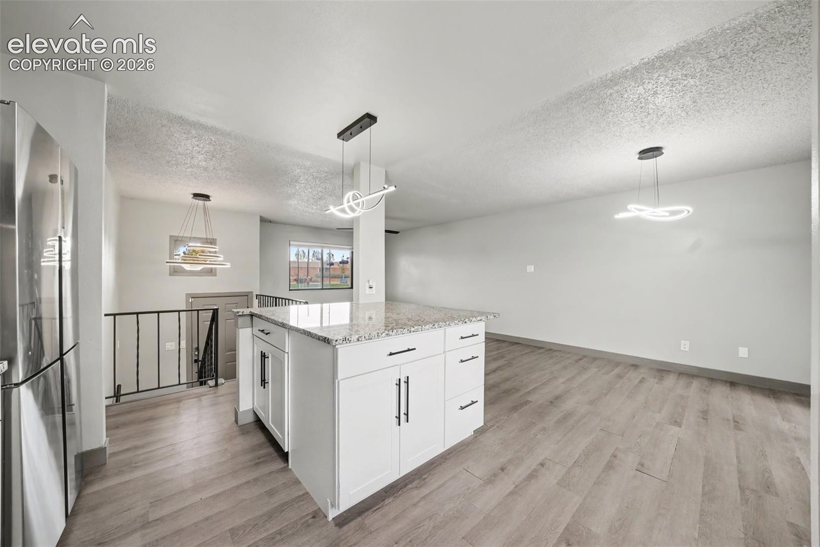 Kitchen featuring white cabinetry, stone-finish countertops, wood-finish flooring, and modern geometric pendant lighting