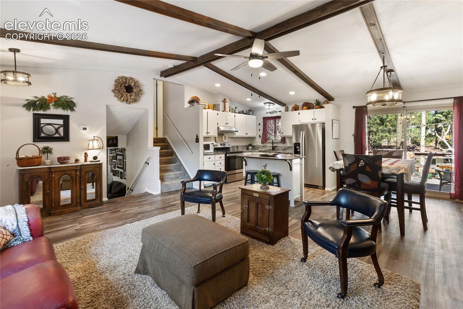 Vaulted ceiling with exposed beams, wood-finish flooring, kitchen island with seating, stainless steel appliances, and sliding glass door
