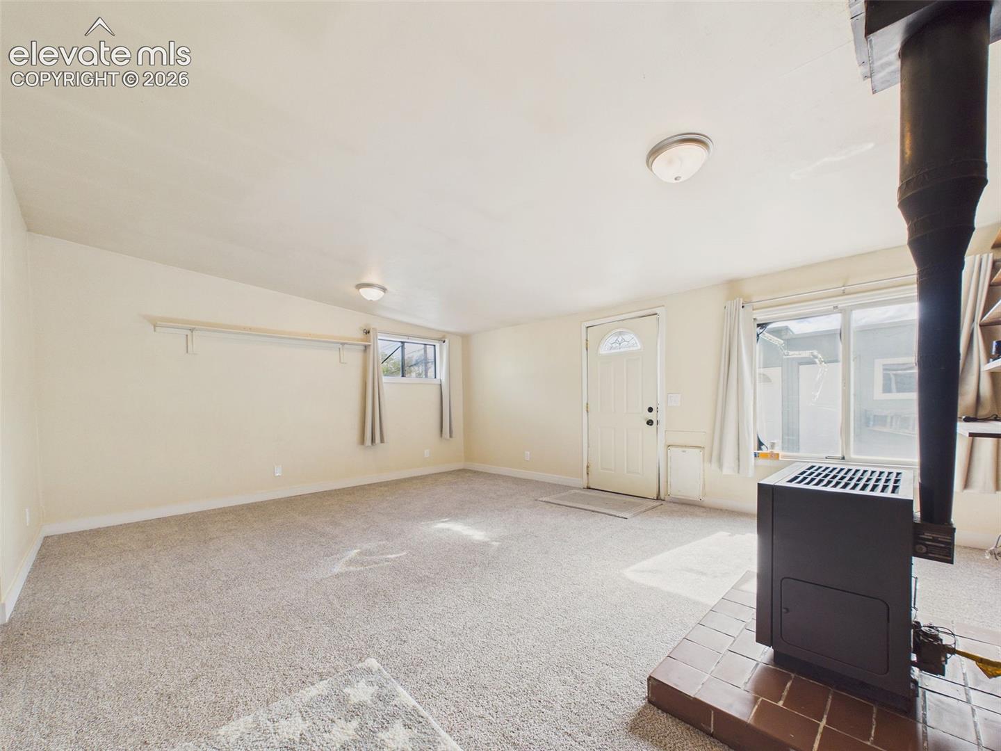 Generously sized family room with carpeting, multiple windows, and a freestanding gas heater situated on a raised brick hearth.