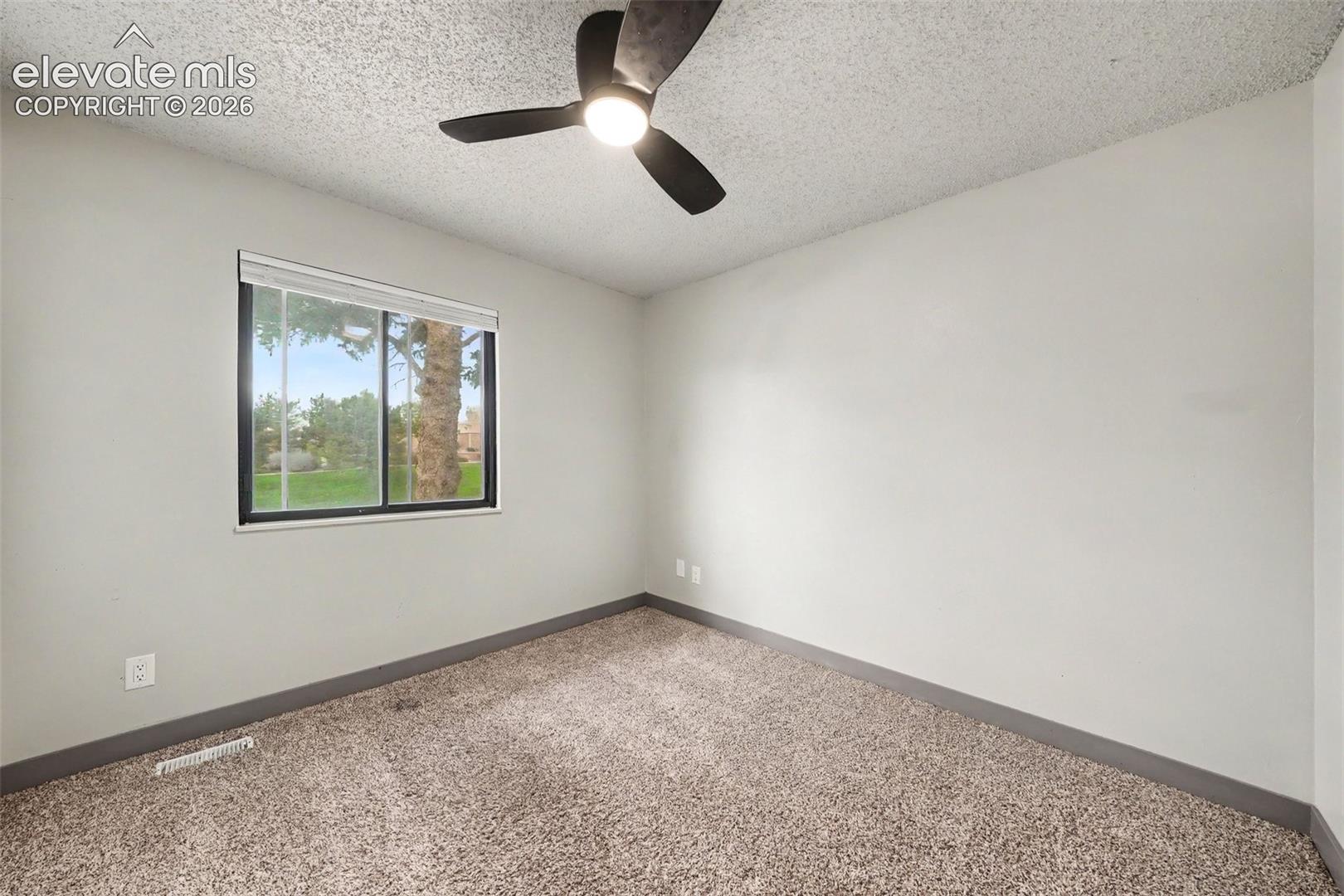 Interior space featuring neutral wall tones, carpeted flooring, a sliding window with exterior greenery, and a ceiling fan with integrated lighting