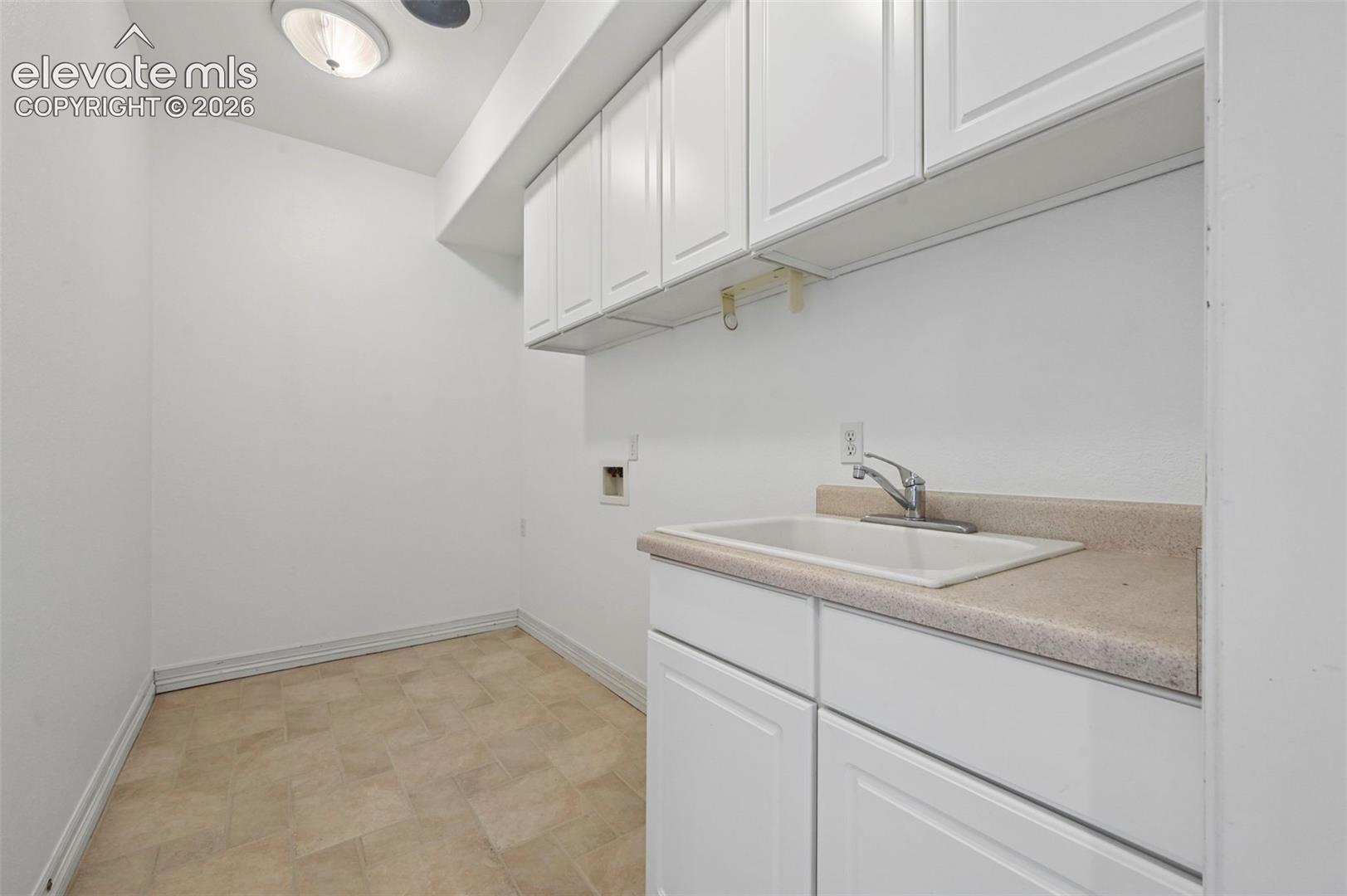 Utility room featuring a utility sink, light beige countertop, and white cabinetry