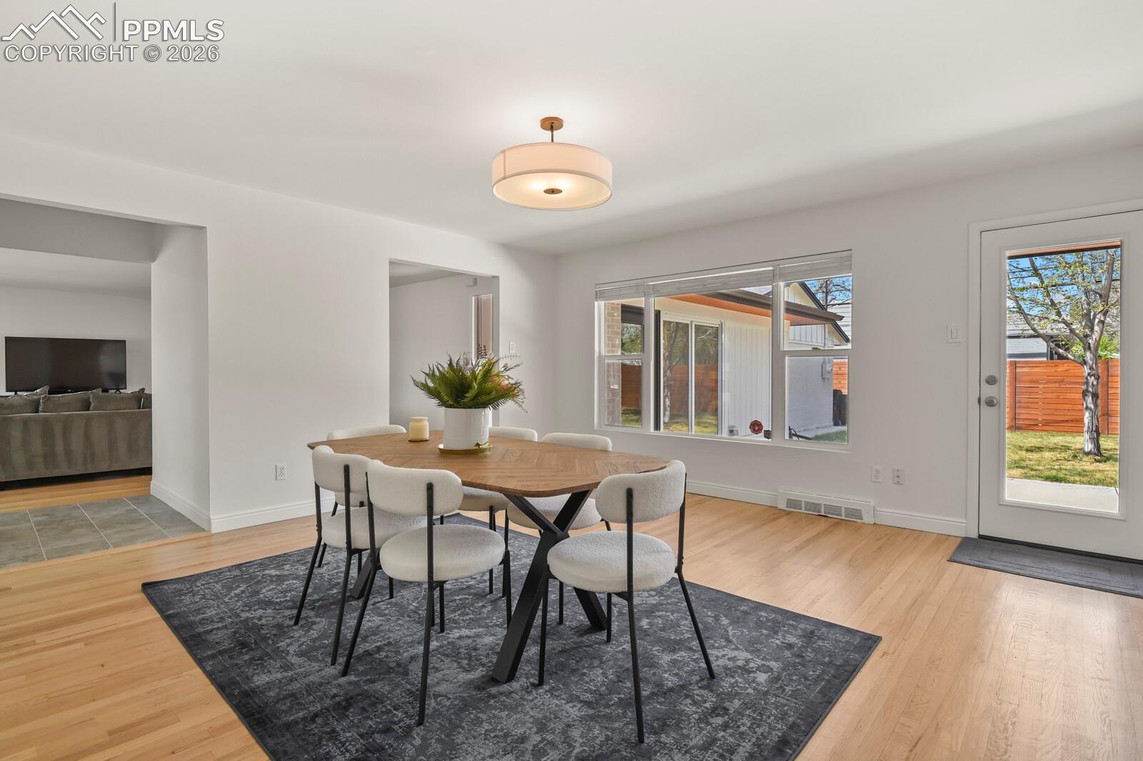 Dining area featuring hardwood flooring, ample natural light through a large picture window and a door opening to a private backyard