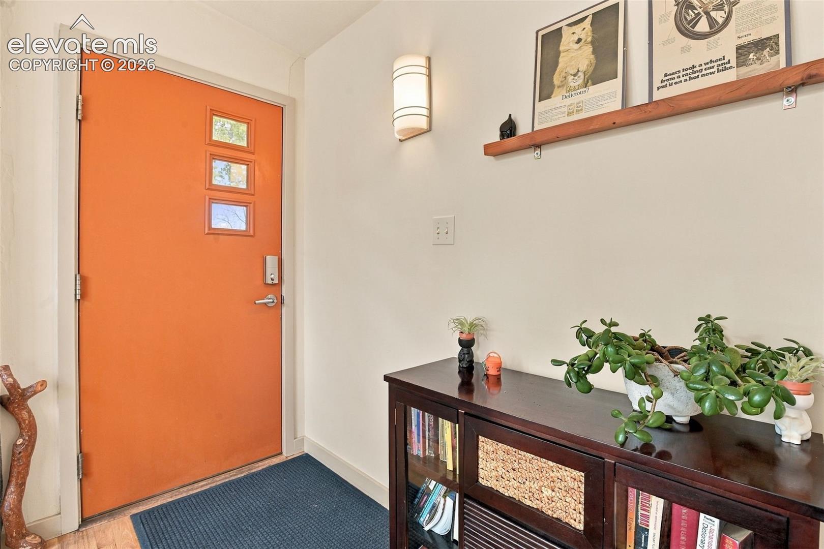 Entryway featuring a solid door with triple-lite glass inserts, a wall-mounted sconce, and a natural wood floating display shelf