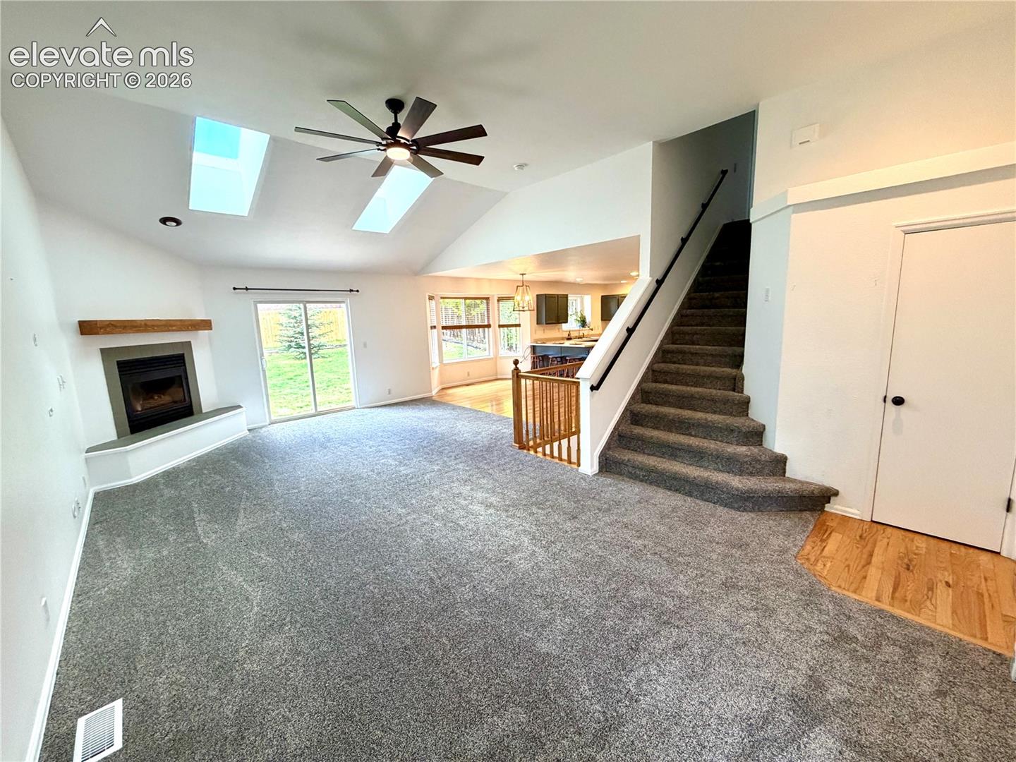 Vaulted living room featuring a corner fireplace with a wood mantle, two skylights, a ceiling fan, and sliding glass doors opening to the exterior
