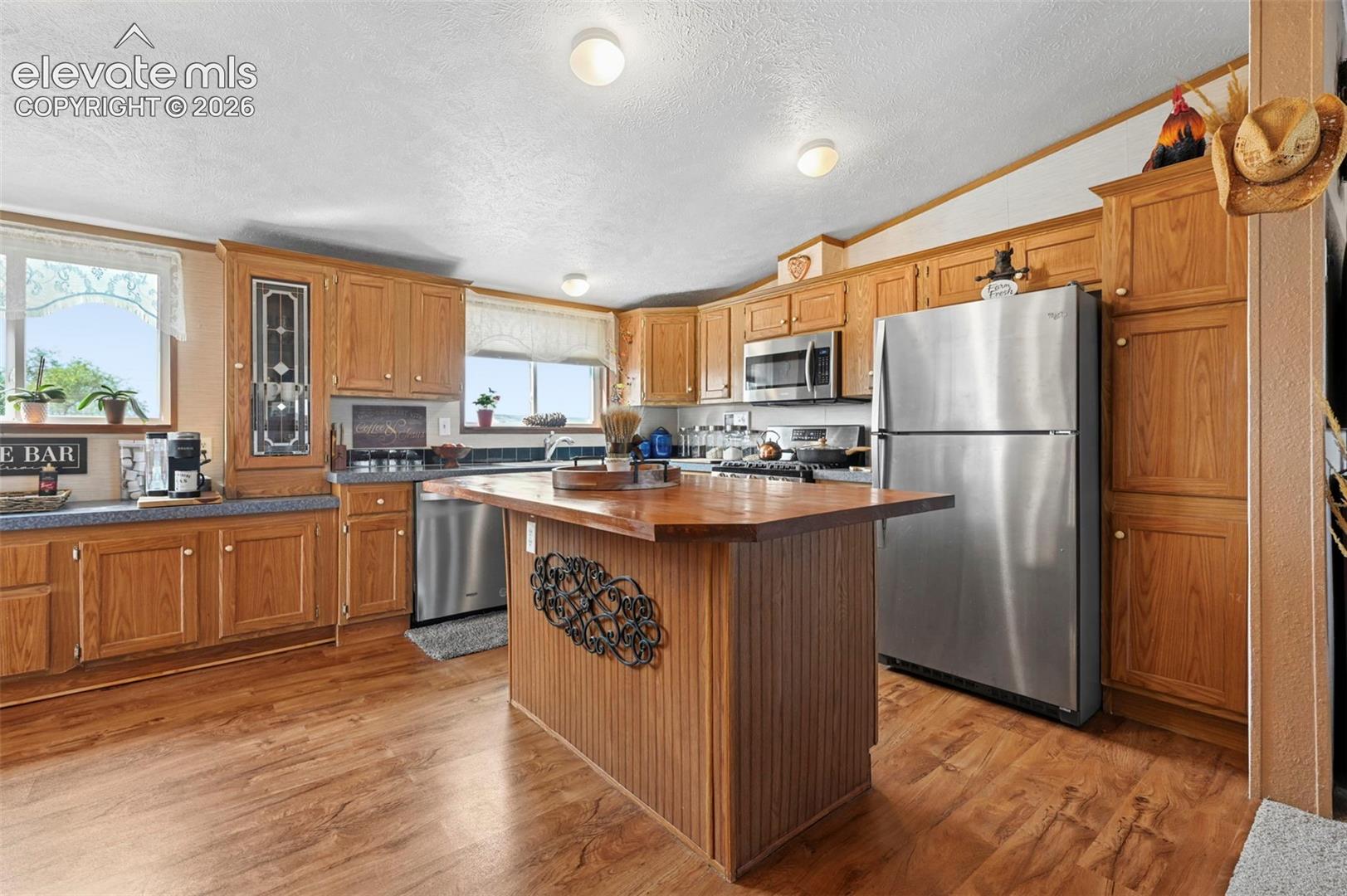 Kitchen featuring wood cabinetry, stainless steel appliances, wood-finish flooring, a central island with a wood countertop, and inset decorative cabinet glass