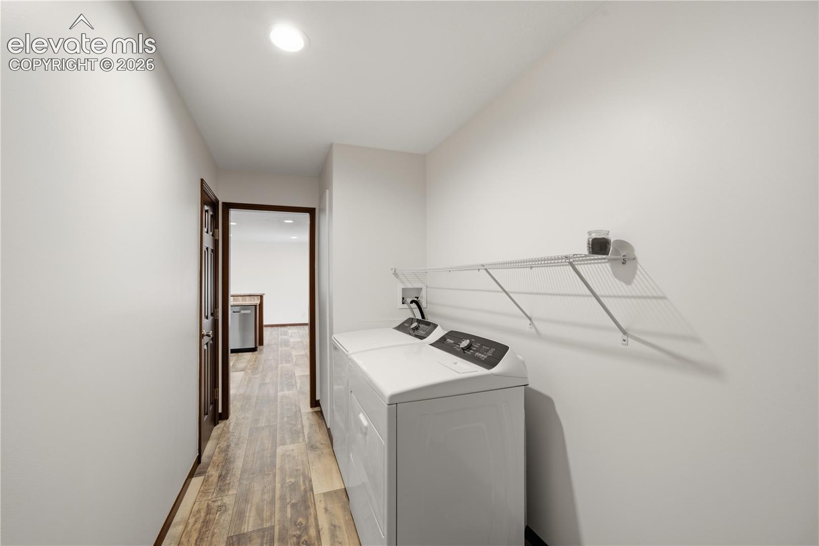 Laundry area featuring wood-finish flooring, white walls, and a wire storage shelf