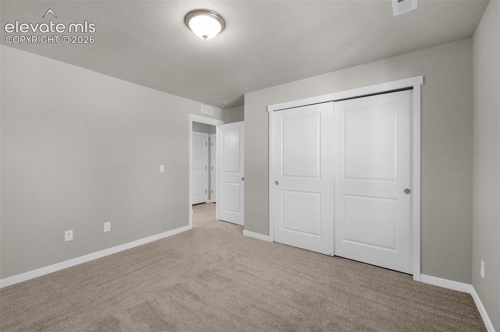 Neutral interior featuring wall-to-wall carpeting, flush-mount ceiling lighting, and sliding-panel closet doors with white trim