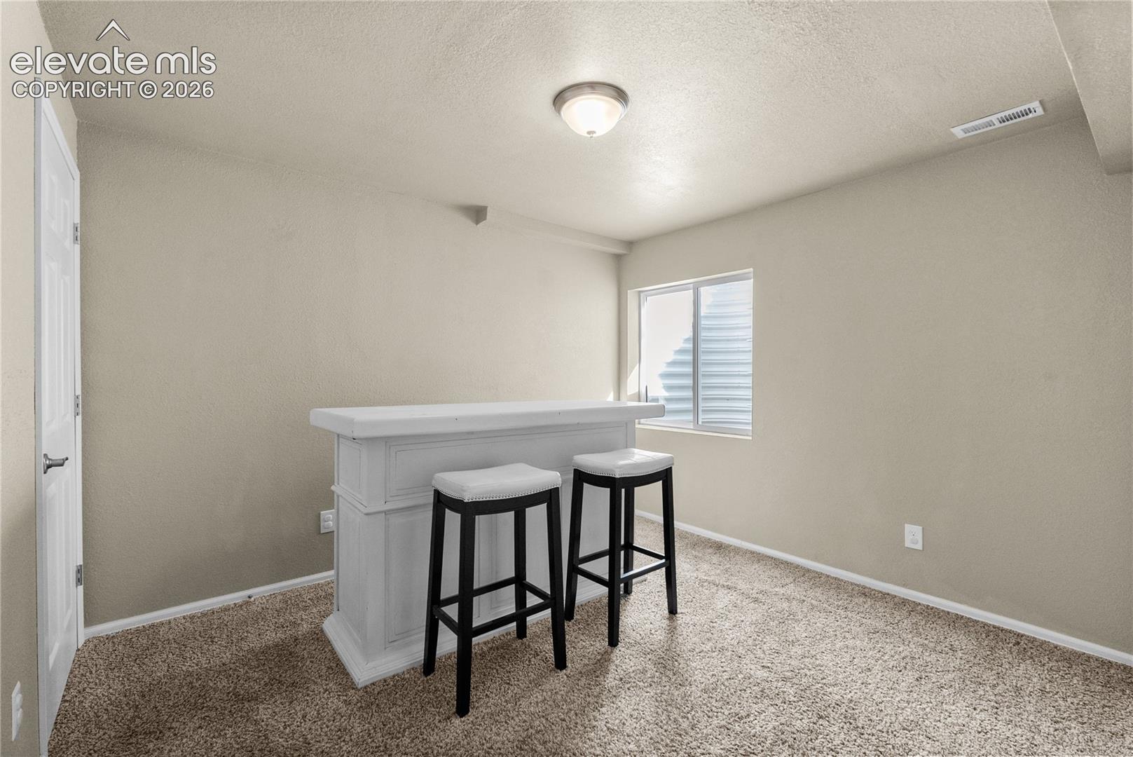 Integrated bar counter, window with privacy blinds, neutral wall paint, and ceiling-mounted light fixture