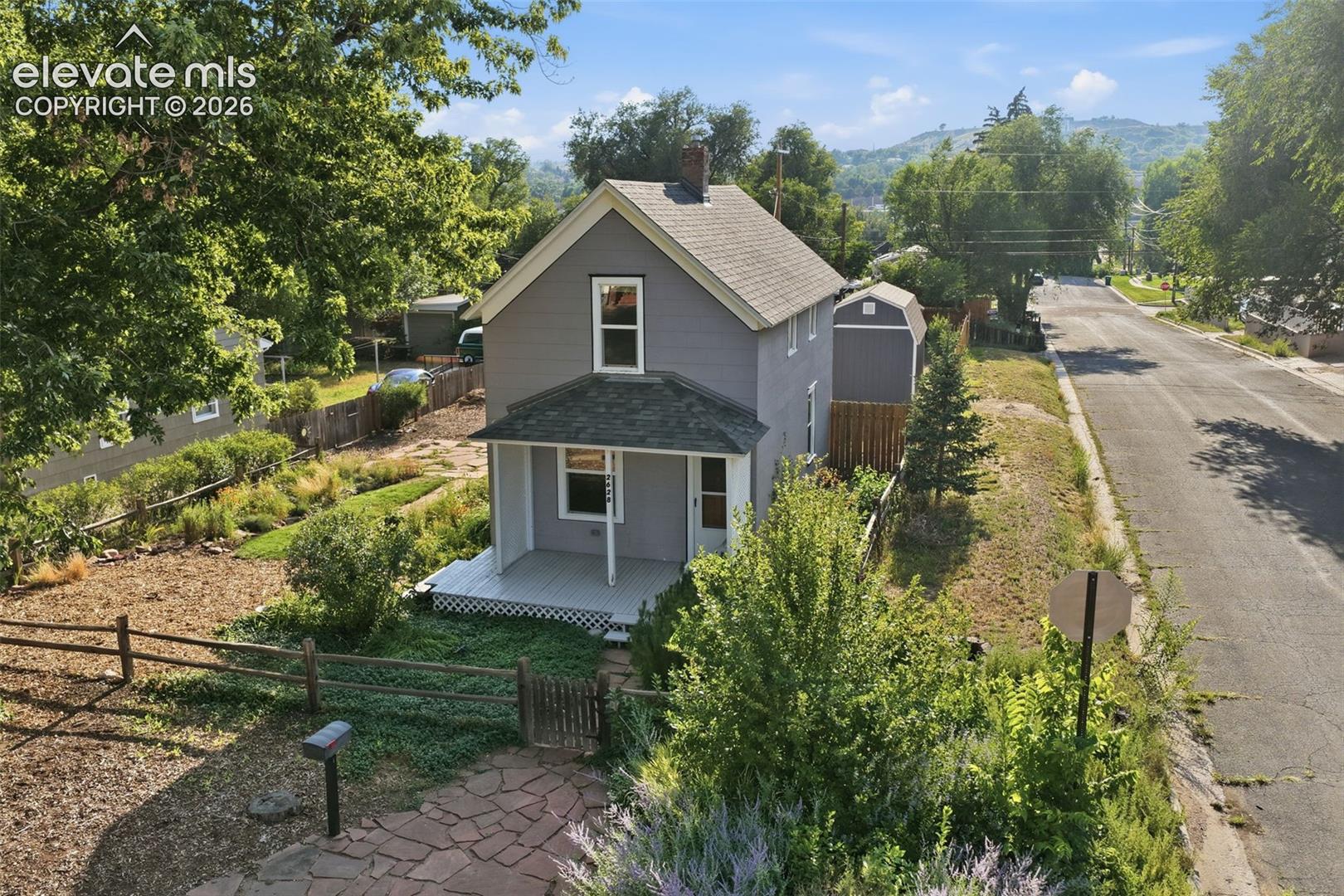 Gray siding exterior with white trim, covered front porch, stone pathway, mature trees, and mountainous backdrop.