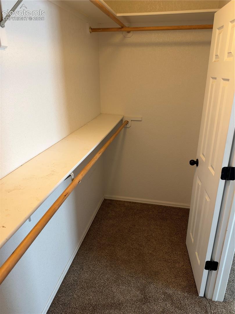 Walk-in closet featuring dual-level wooden hanging rods, upper shelving, textured carpeting, and a white six-panel door with matte black hardware