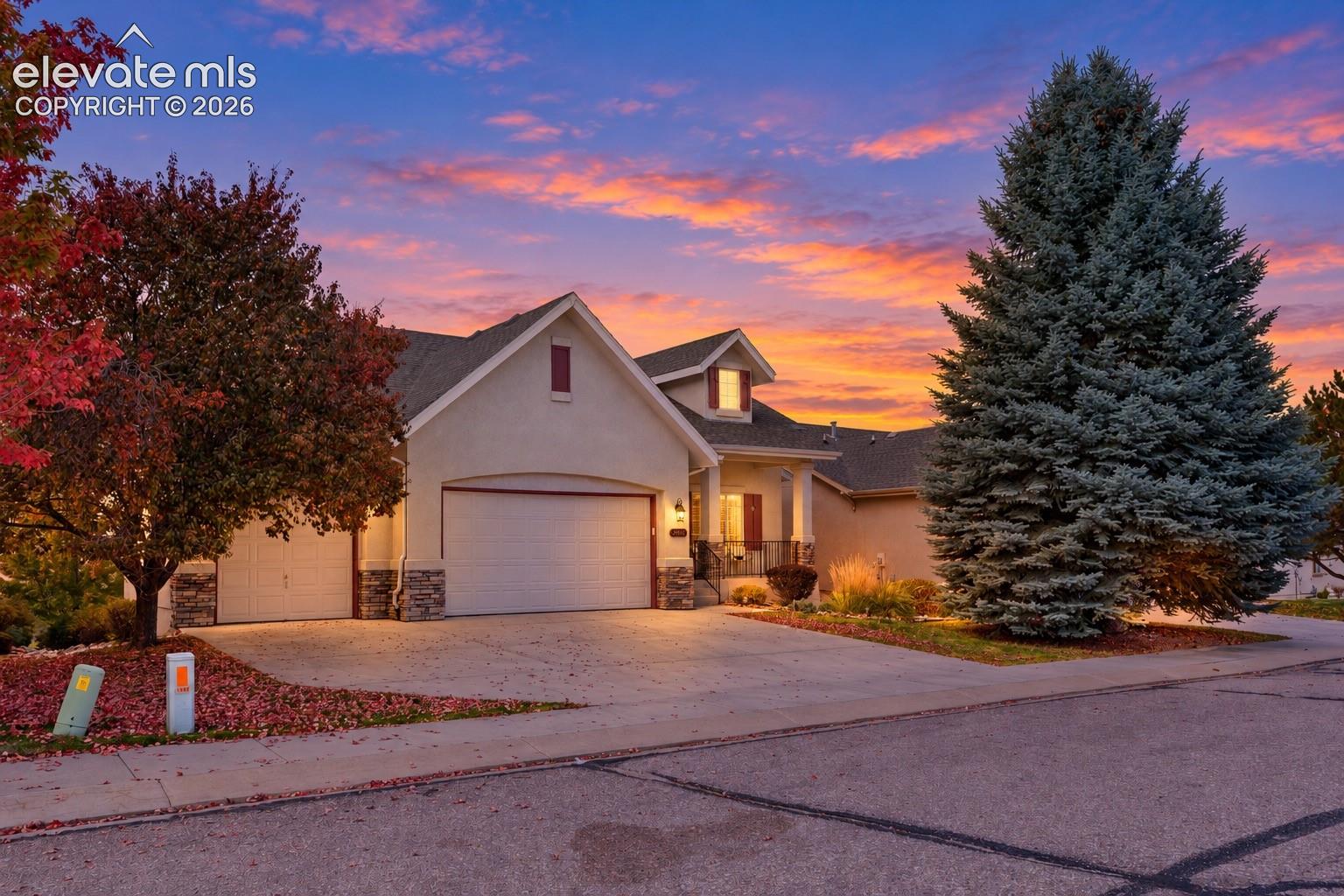 Exterior facade featuring a three-car garage, stone veneer siding, gable rooflines, and concrete driveway