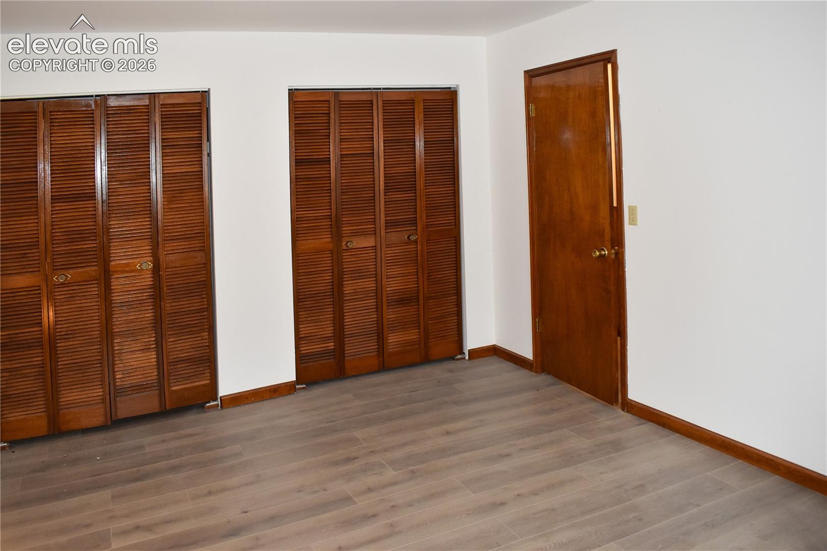 Wood-finish flooring, white wall paint, two sets of louvered bi-fold closet doors, and a wood-panel interior door