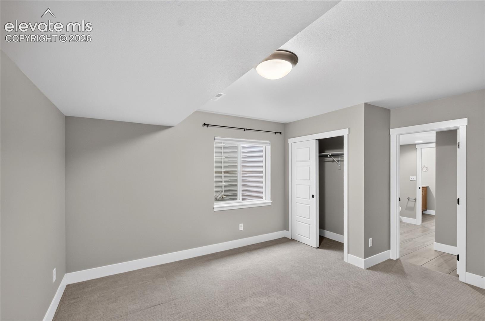 Carpeted room featuring light gray walls, white trim, a flush-mount ceiling light, and a window with horizontal blinds