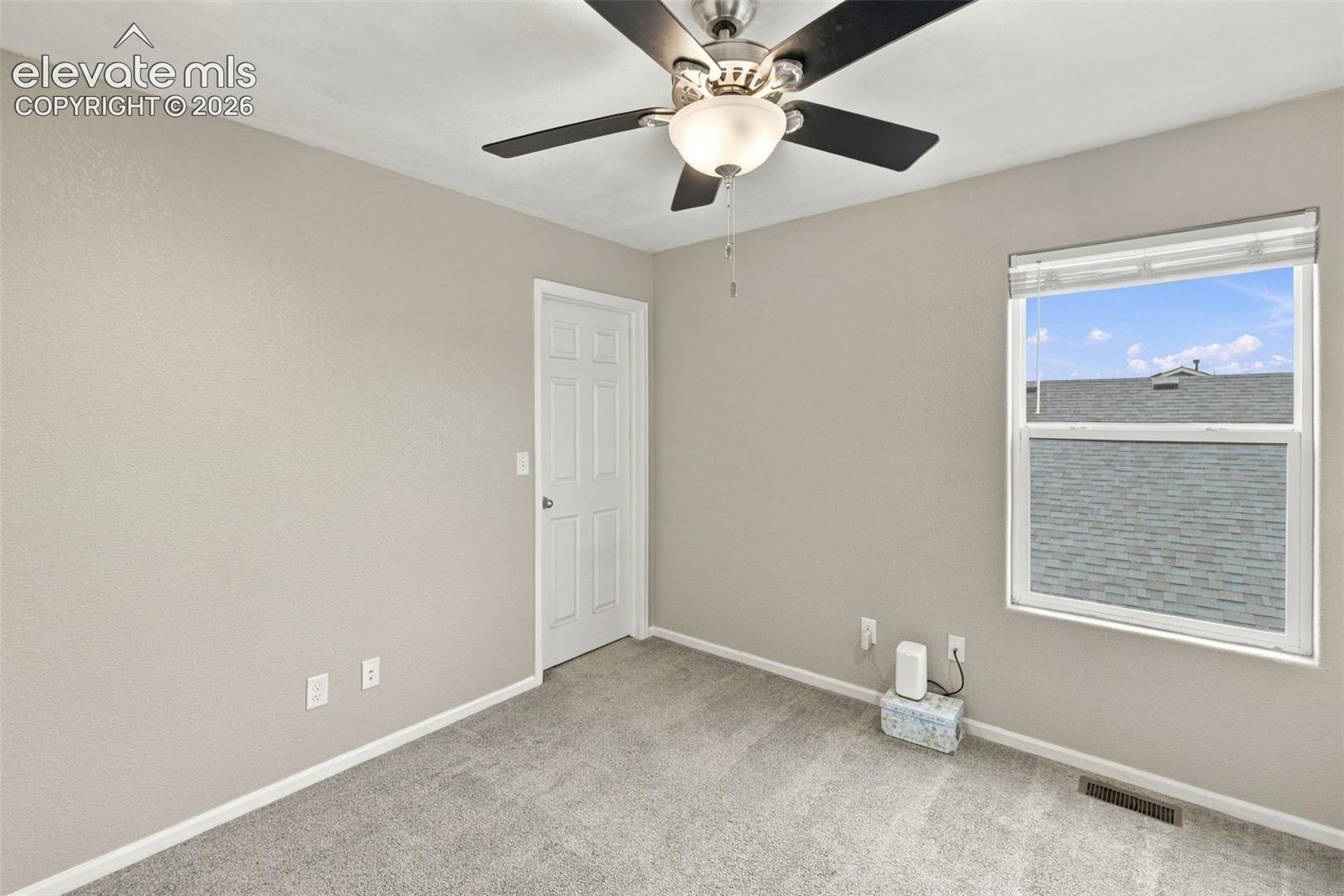 Neutral-toned interior featuring wall-to-wall carpeting, a multi-blade ceiling fan with an integrated light fixture, a single-panel interior door, and a single-hung window with white framing