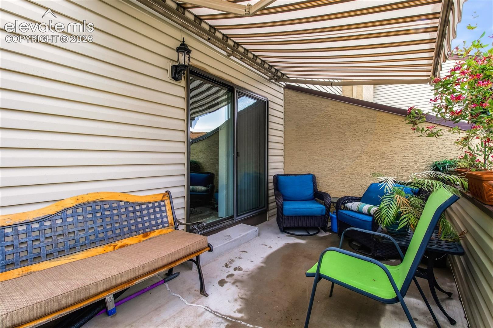 Concrete patio featuring a retractable fabric awning, sliding glass door, and exterior wall-mounted lighting