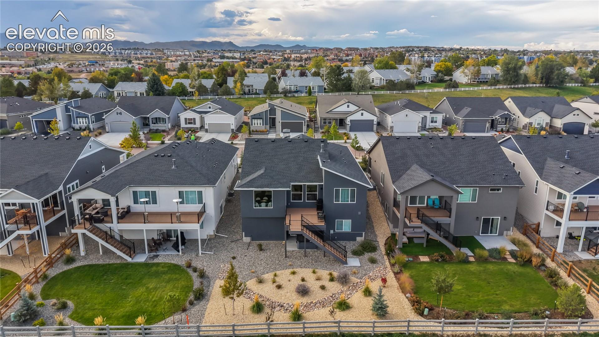 Aerial exterior featuring elevated rear wood-finish decks, tiered staircases with metal railings, gravel and grass landscaping, and perimeter wood fencing against a mountain backdrop
