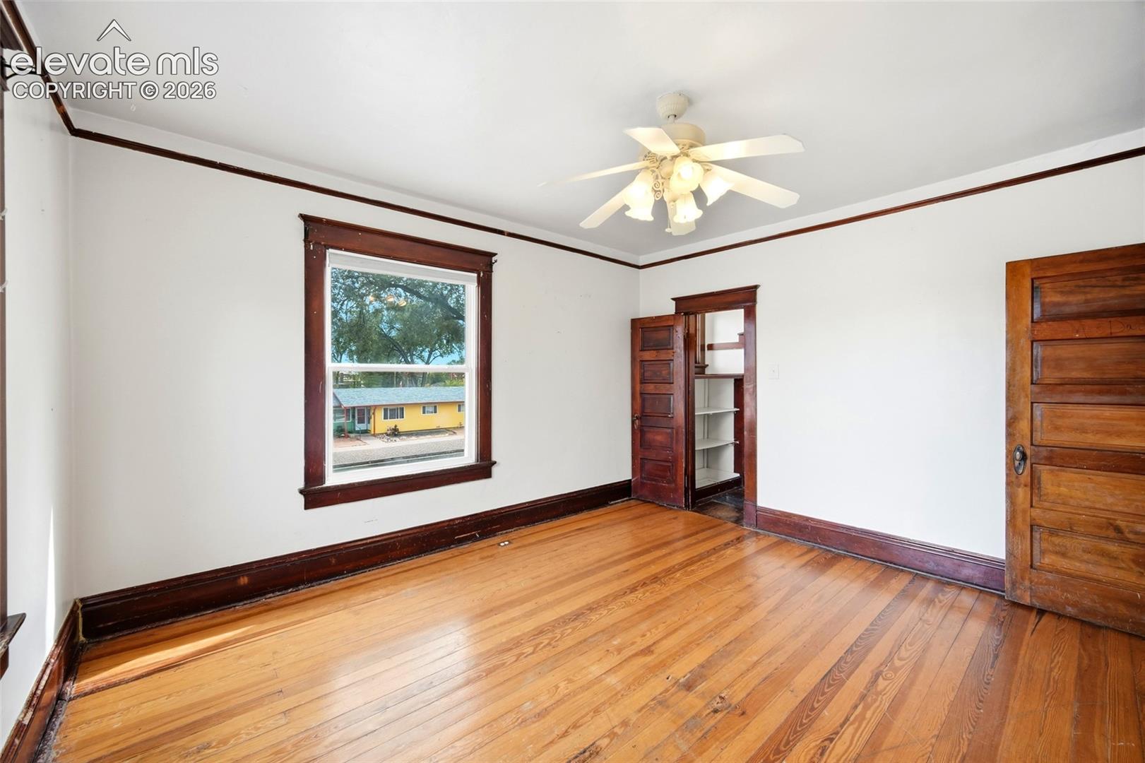 Room featuring natural wood-finish flooring, stained wood door and window trim, a five-panel wood door, and a ceiling-mounted light fixture with a fan
