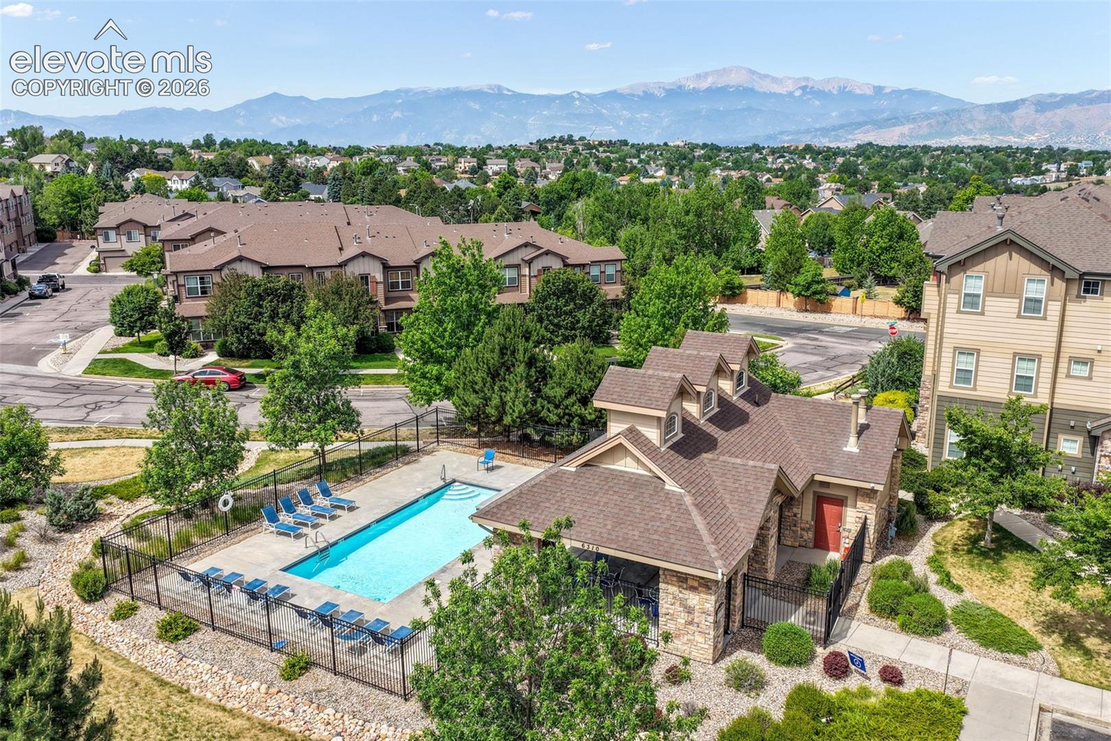 Outdoor swimming pool with surrounding fencing, adjacent clubhouse with dormer windows, and a paved sidewalk
