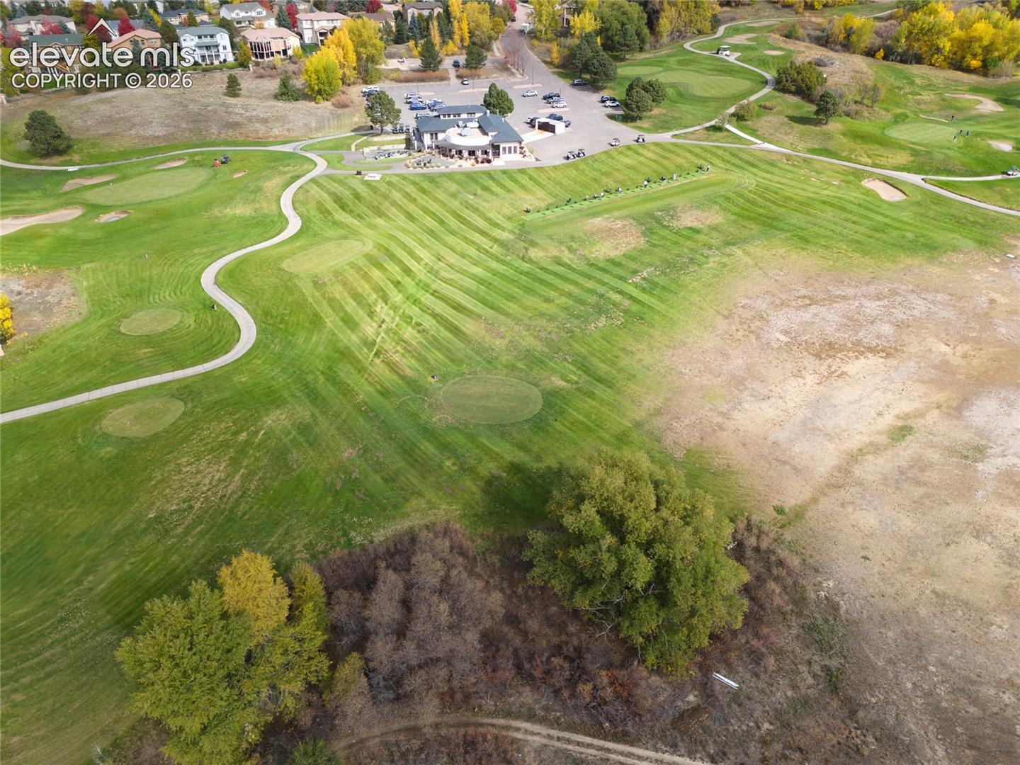 Aerial perspective featuring a sprawling golf course, manicured fairways, paved cart paths, and mature trees