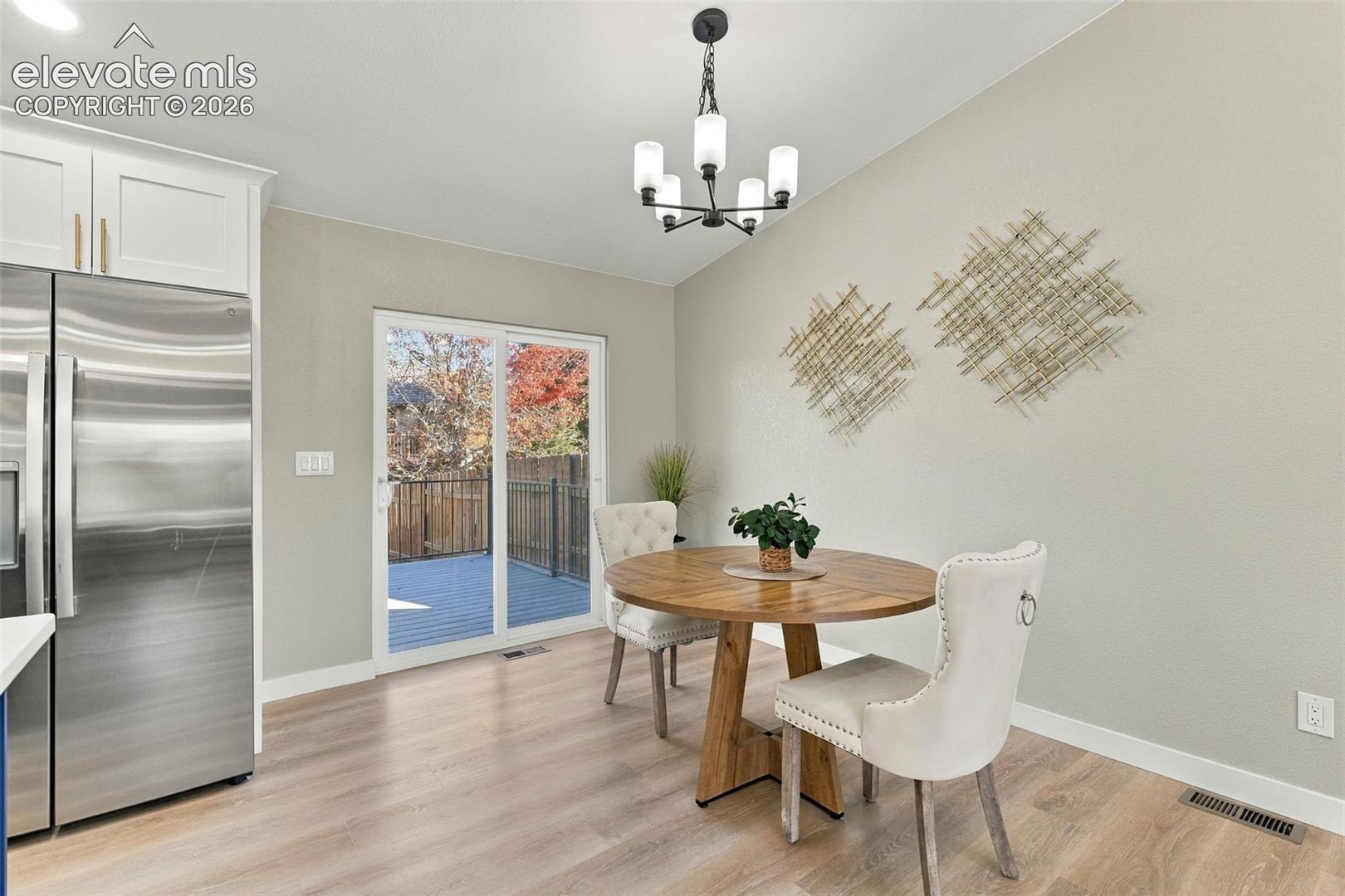 Dining area featuring wood-finish flooring, white cabinetry, a multi-light chandelier, and sliding glass doors leading to an outdoor deck