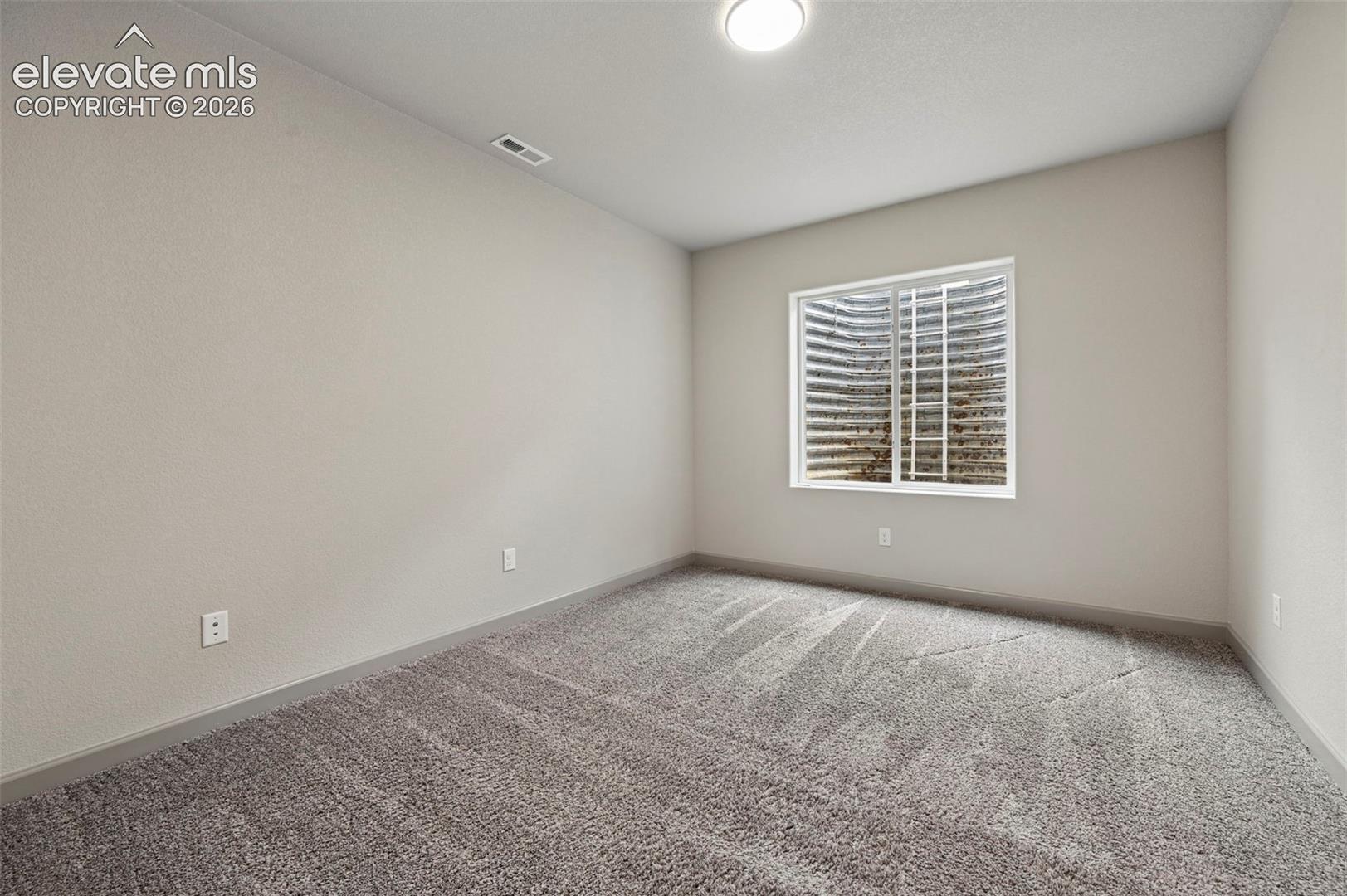 Neutral-toned room featuring textured carpeting, smooth wall finish, flush-mount ceiling light, and an egress window with a metal window well