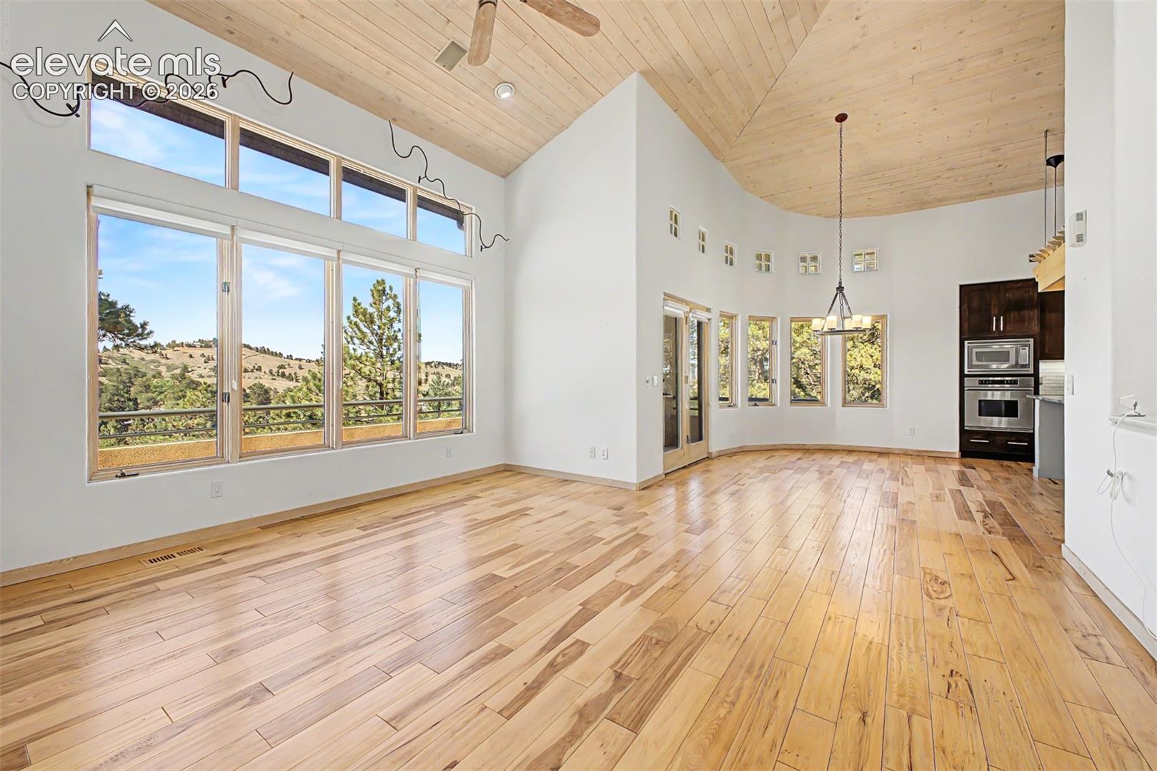 Vaulted wood-paneled ceilings, expansive window wall with transoms, wood-finish flooring, built-in stainless steel appliances, and a contemporary chandelier