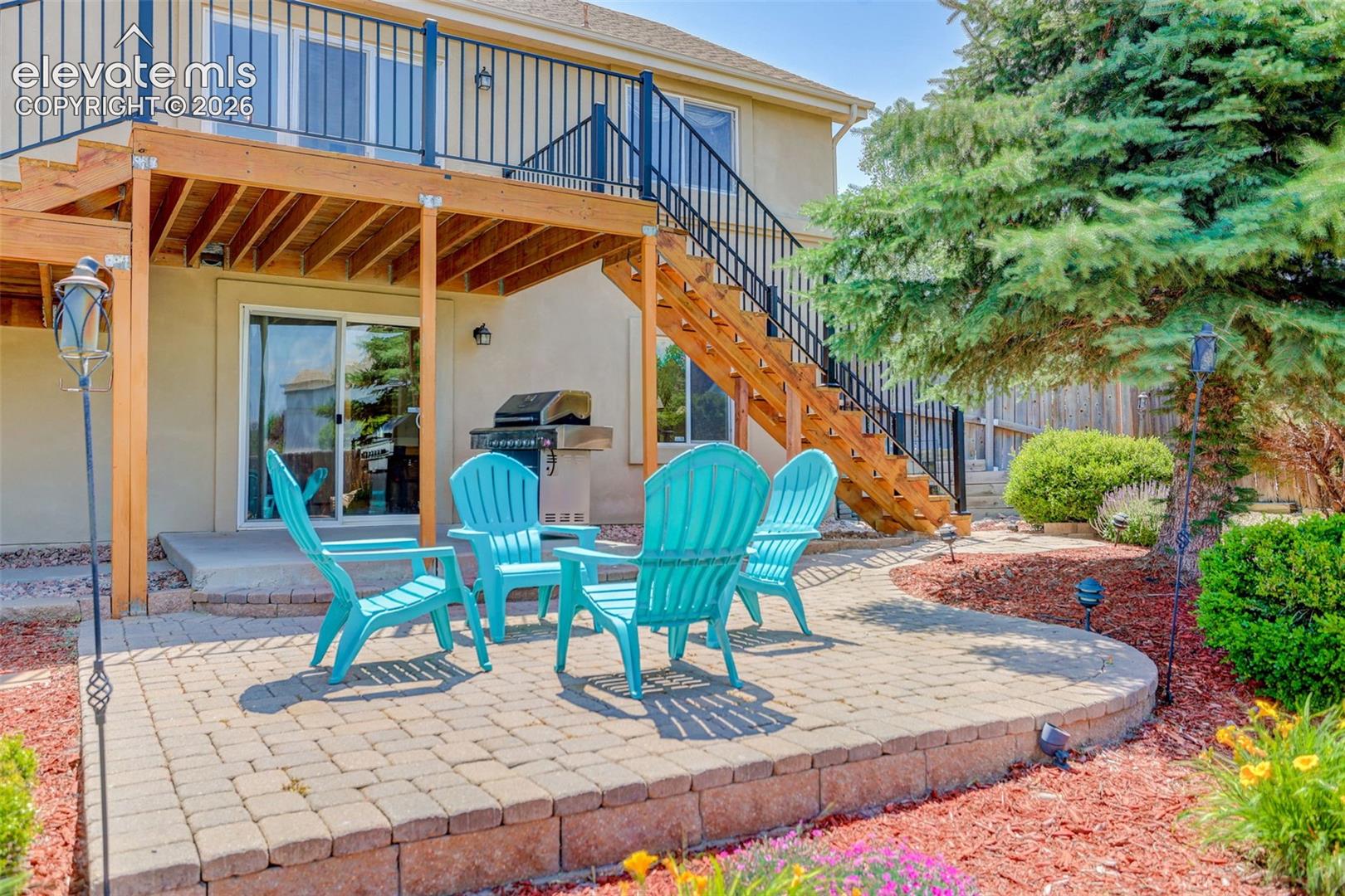 Outdoor living space featuring a paver patio with a retaining wall, a multi-level wood deck with black metal railings, and mature landscaping