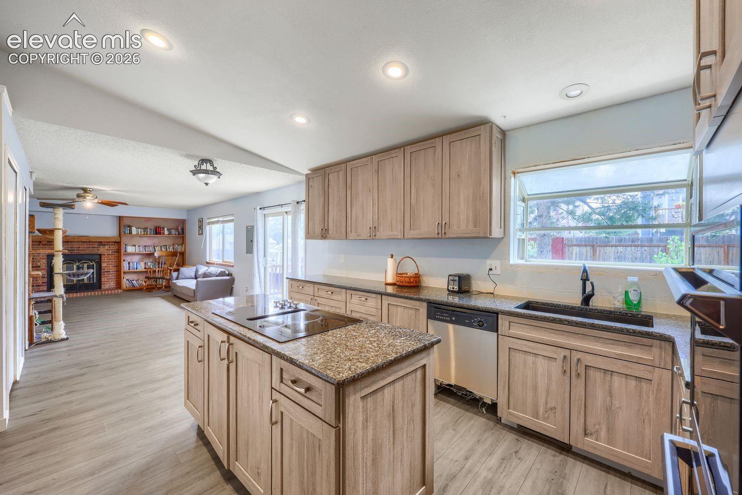 Kitchen featuring an island with built-in cooktop, light wood-finish cabinetry, stone countertops, and stainless steel appliances