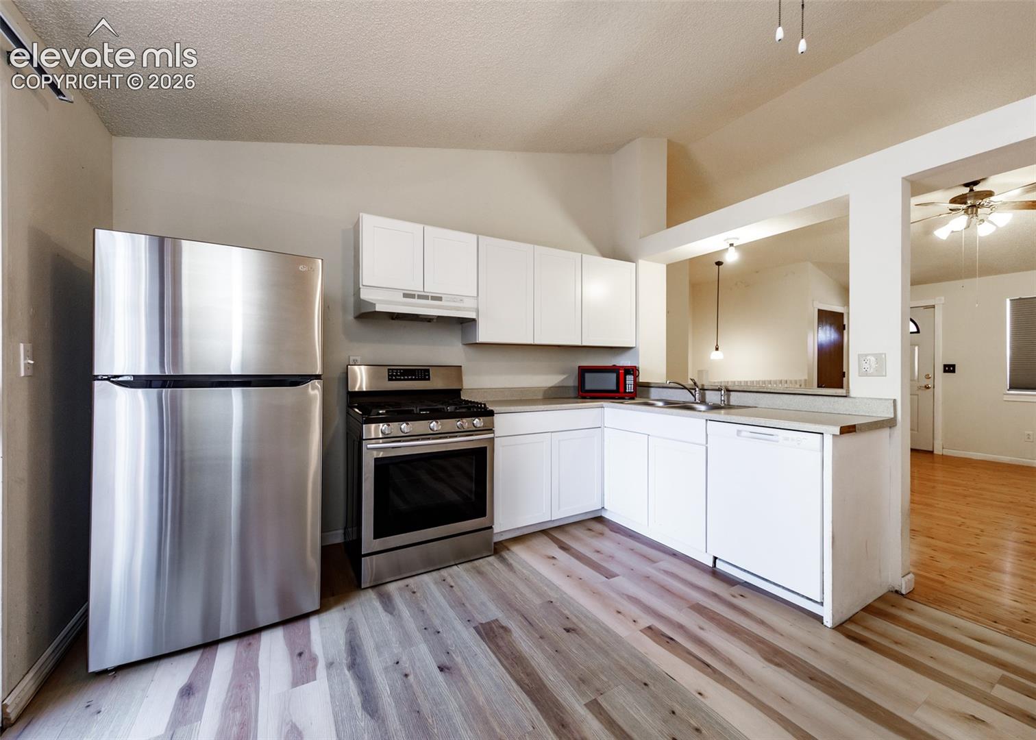 Kitchen featuring white cabinetry, wood-finish flooring, stainless steel gas range, and stainless steel refrigerator