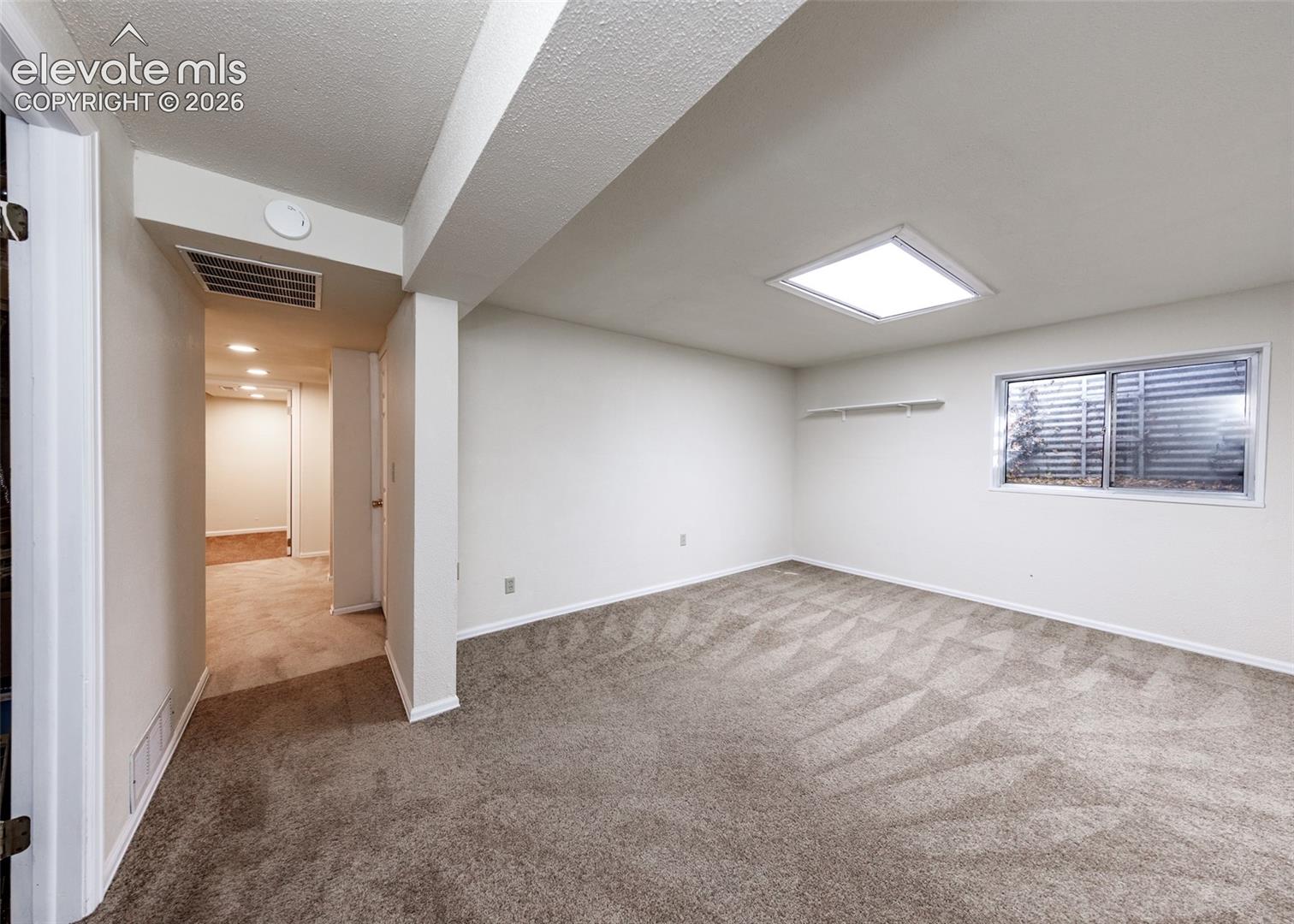 Neutral interior space featuring carpeted flooring, a recessed ceiling light fixture, a horizontal sliding window, and a built-in wall shelf