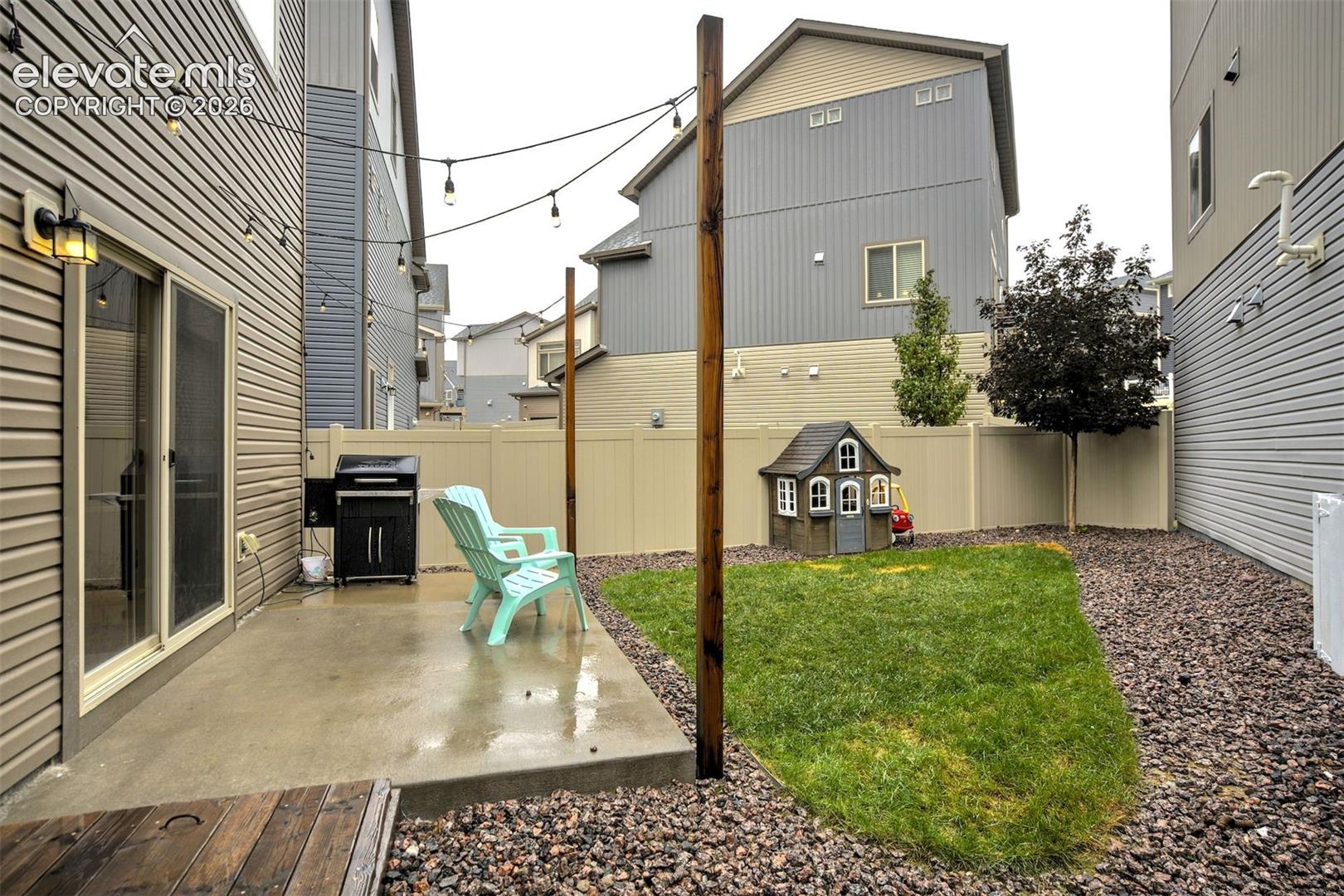 Rear yard featuring a concrete patio, perimeter vinyl fencing, and overhead string lighting