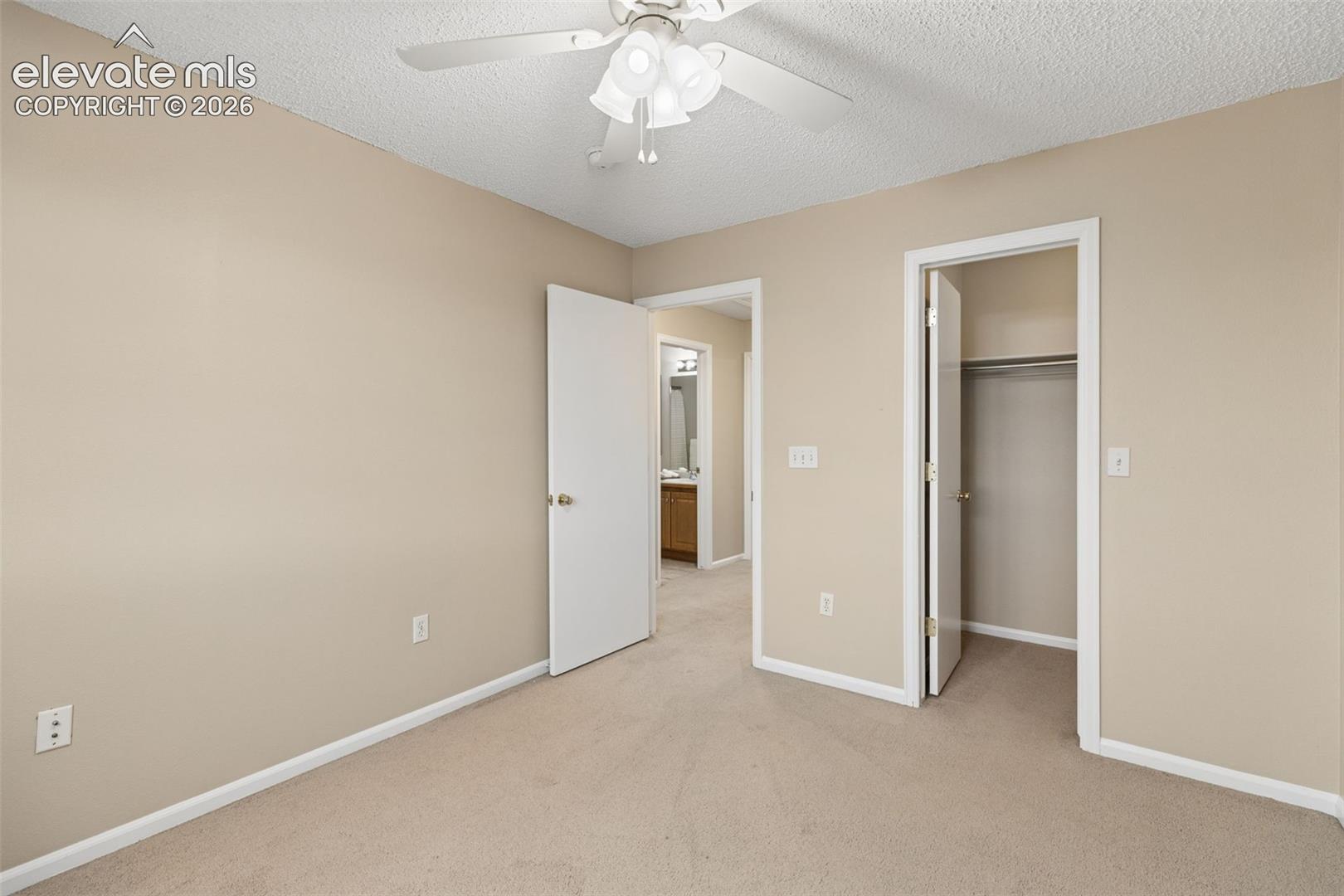 Neutral-toned room featuring carpeted flooring, a ceiling fan with integrated lighting, and a closet with a built-in rod