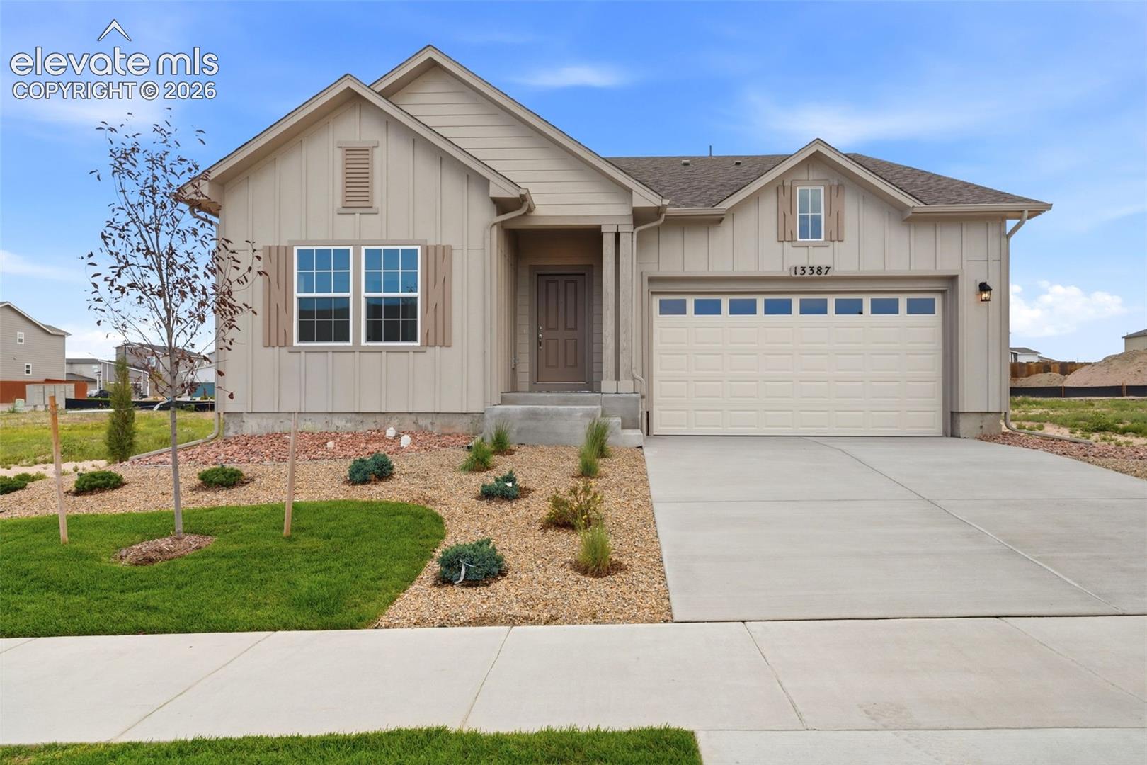 Board-and-batten siding exterior featuring a covered entryway, attached two-car garage, concrete driveway, and xeriscaped front landscaping