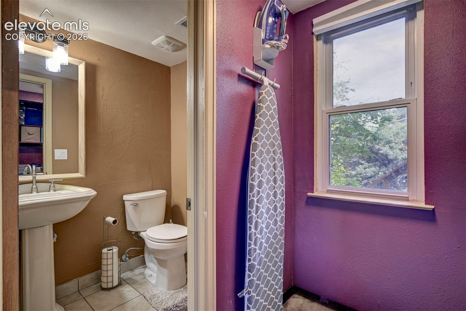 Pedestal sink with chrome faucet, wall-mounted mirror, and overhead lighting fixture