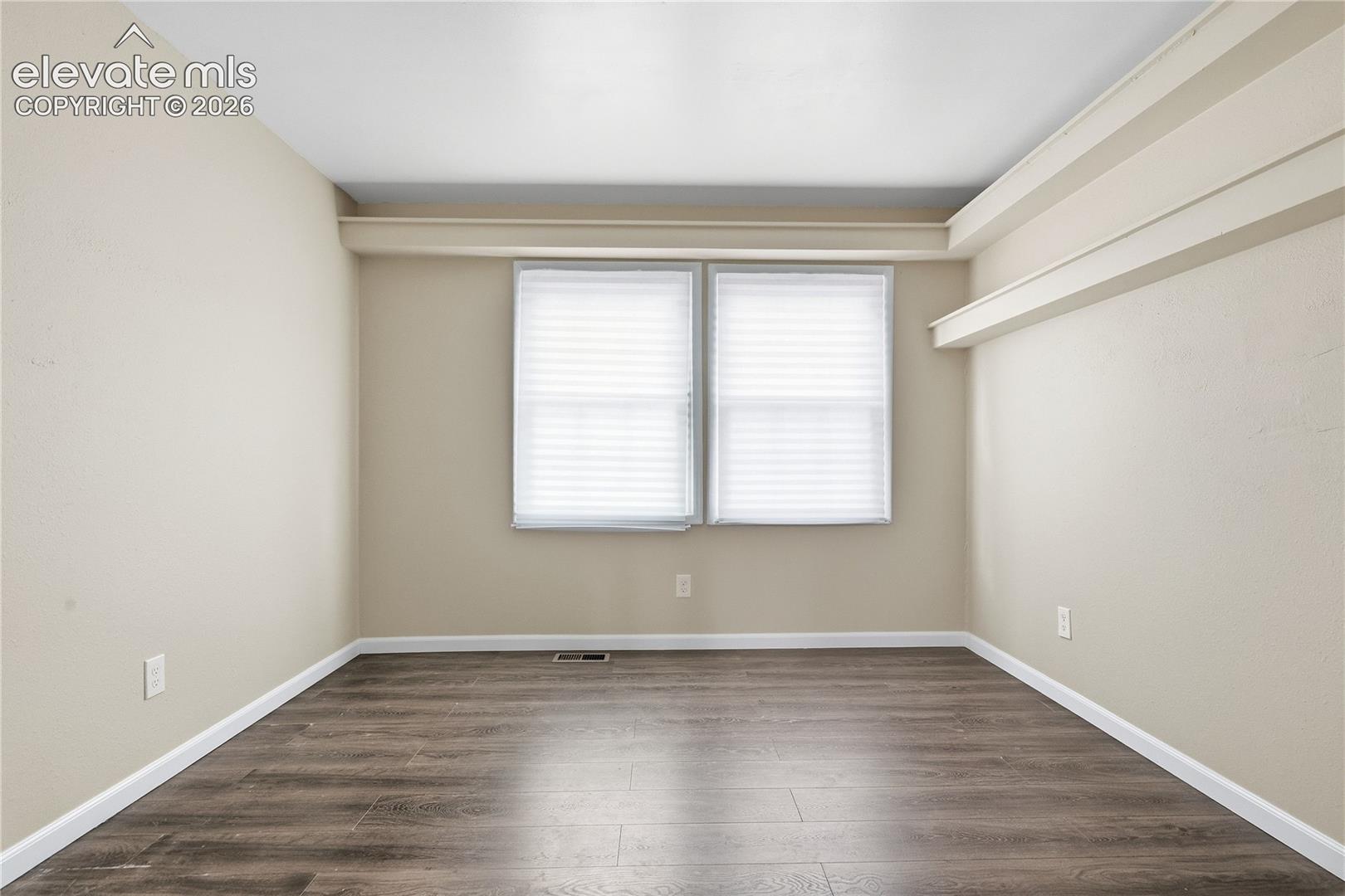 Room featuring wood-finish flooring, neutral wall tones, and two windows
