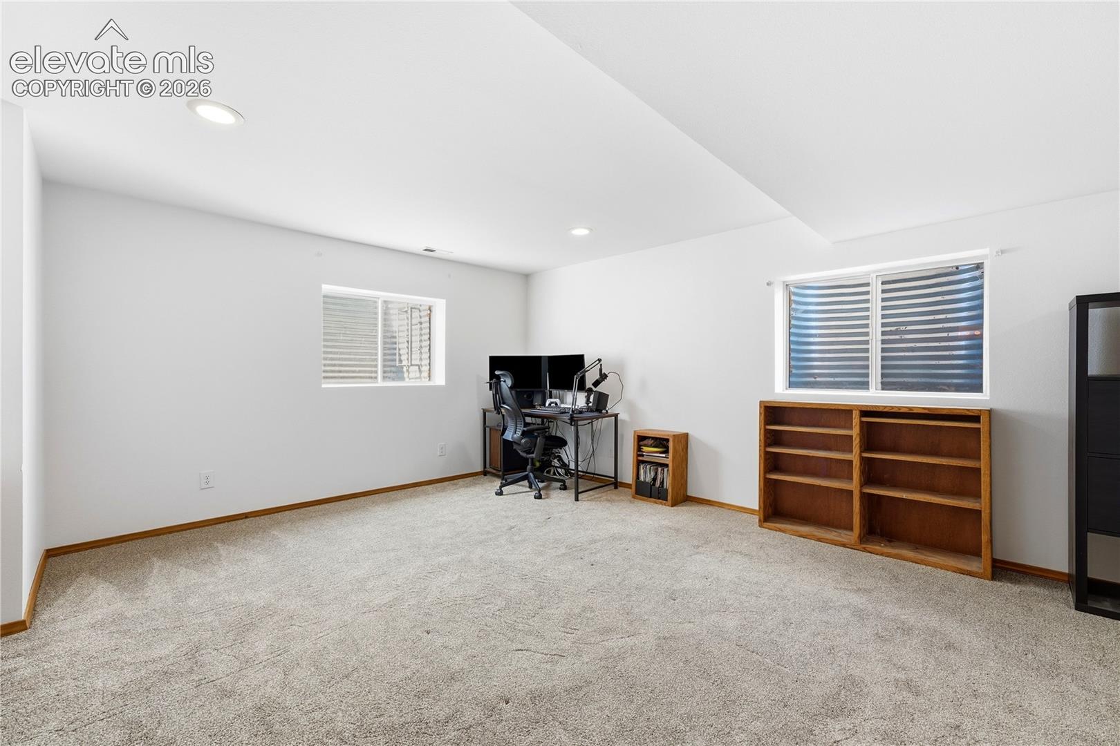 Spacious room featuring light-colored carpeting, white walls, recessed lighting, and window wells