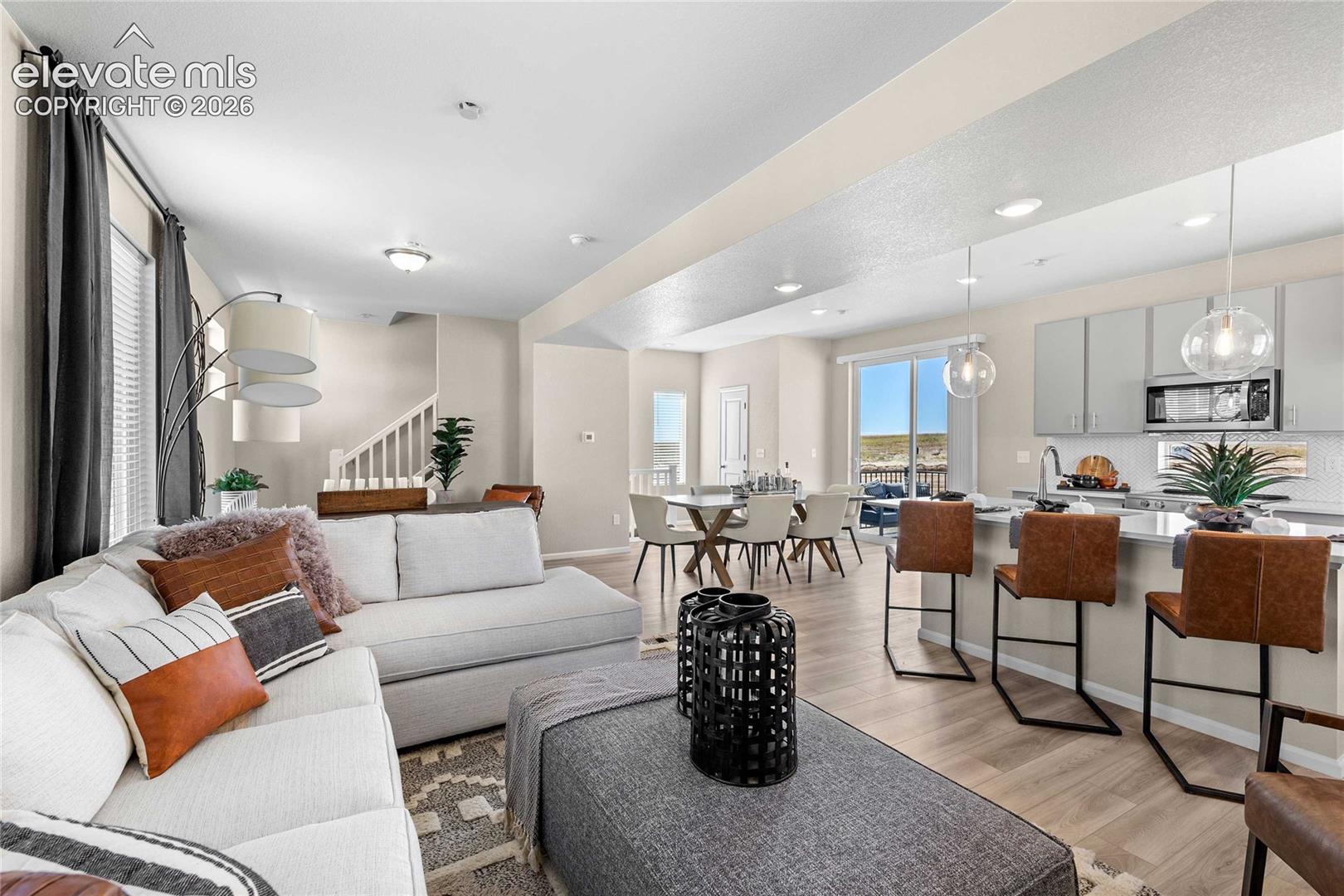 Open-concept floor plan featuring wood-finish flooring, a kitchen island with seating, pendant lighting, and a sliding glass door
*photos of a model home*