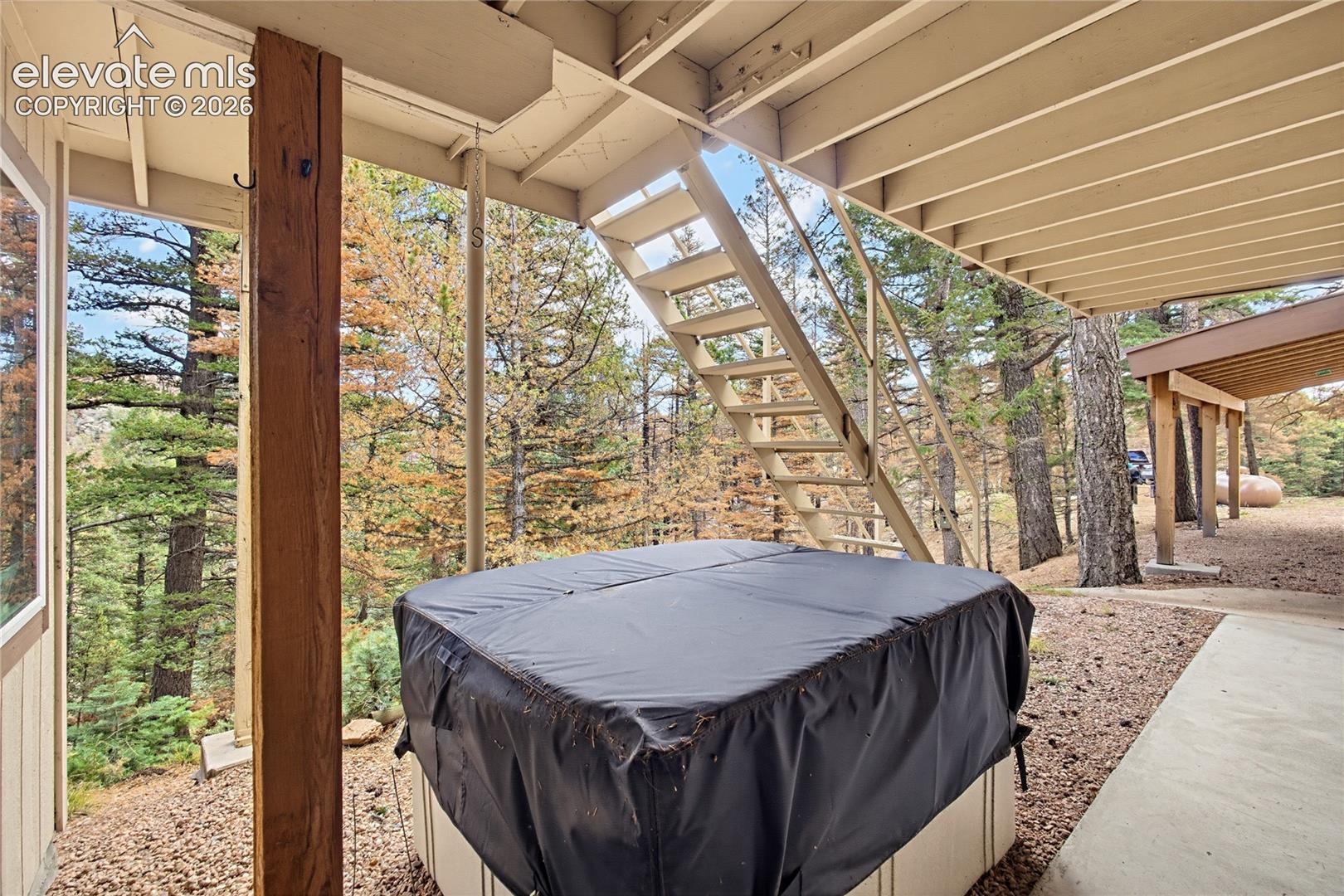 Covered lower deck area featuring a built-in spa, structural wood support columns, metal staircase, and a concrete patio surface