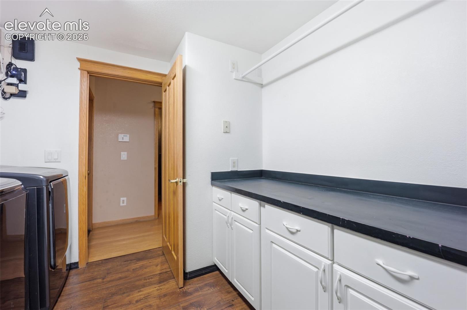 Built-in white cabinetry, dark countertop, wood-finish flooring, and natural wood trim doorway
