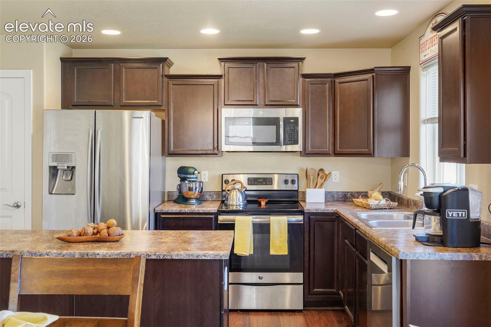 Kitchen featuring dark wood-finish cabinetry, stainless steel appliances, recessed lighting, wood-finish flooring, and a breakfast bar