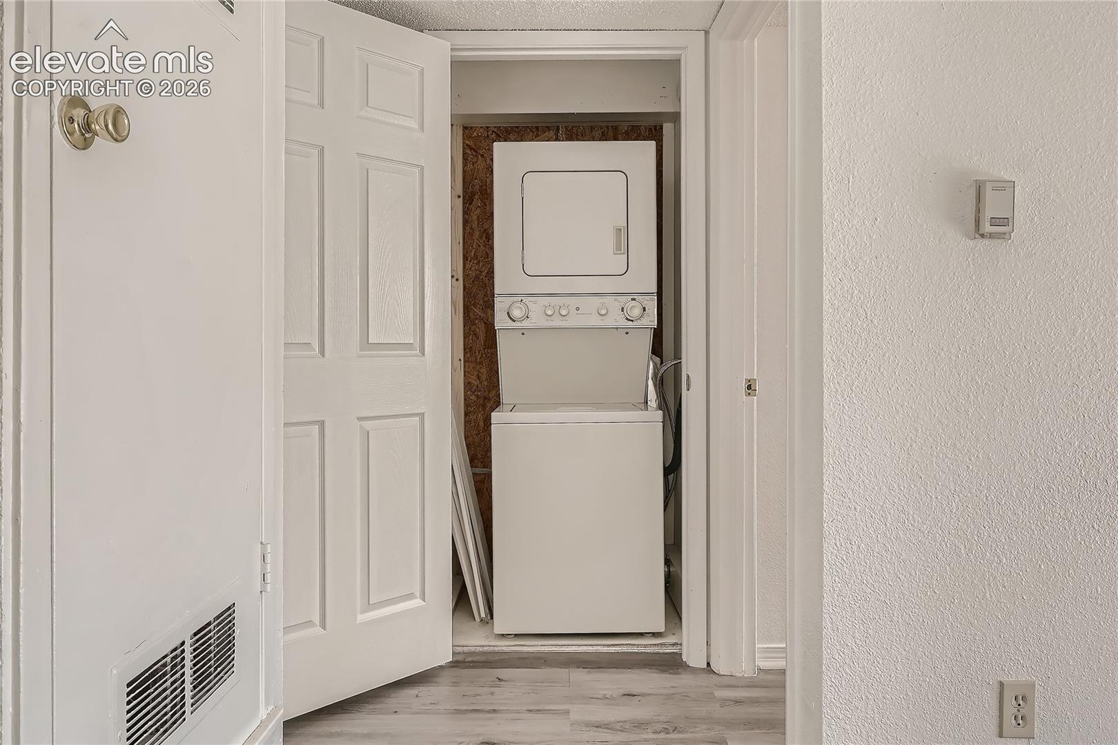 Laundry closet featuring a stackable washer and dryer unit, six-panel interior door, and wood-finish flooring