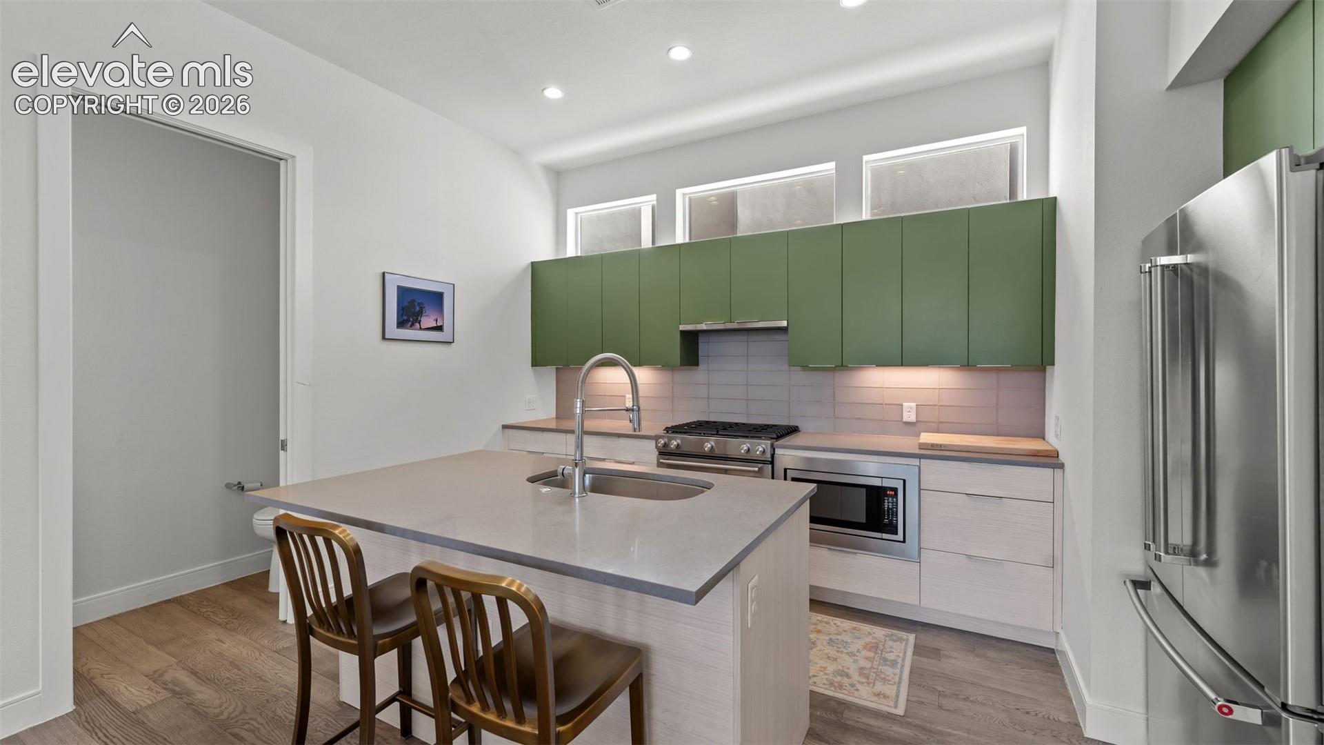 Kitchen featuring sage green upper cabinetry, a central island with a solid-surface countertop and integrated sink, recessed ceiling lighting, clerestory windows, and stainless-steel appliances