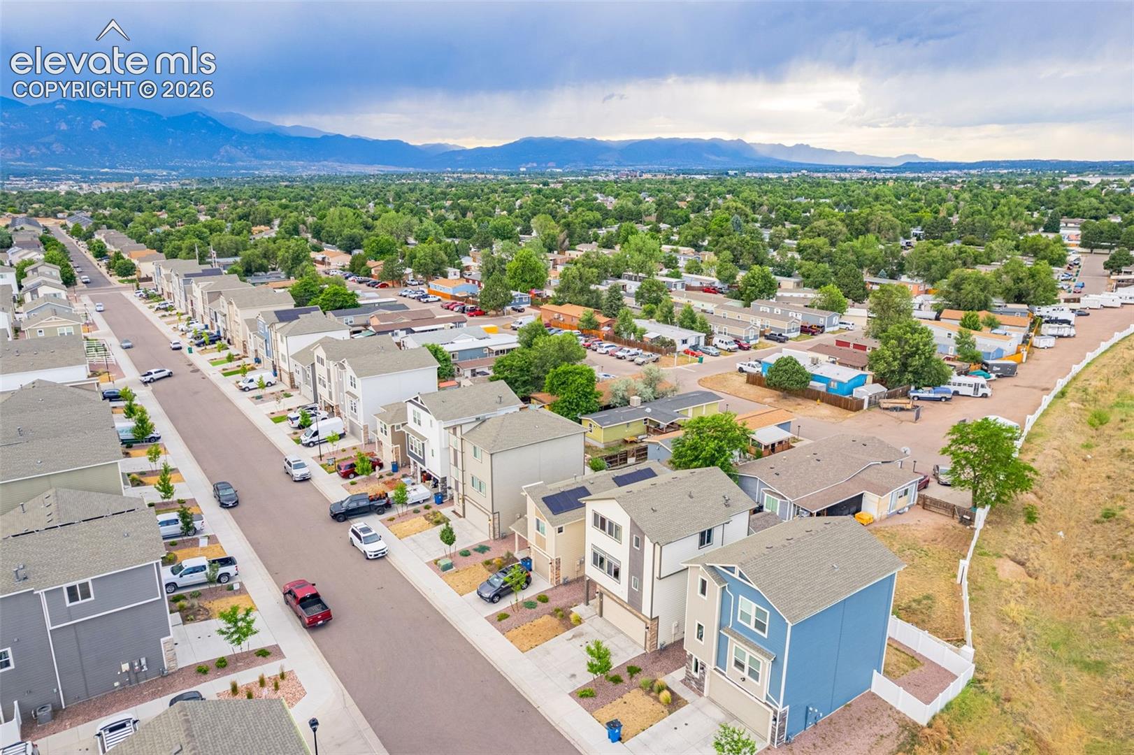 Aerial perspective showcasing a residential area with street parking, established landscaping, and mountain backdrop