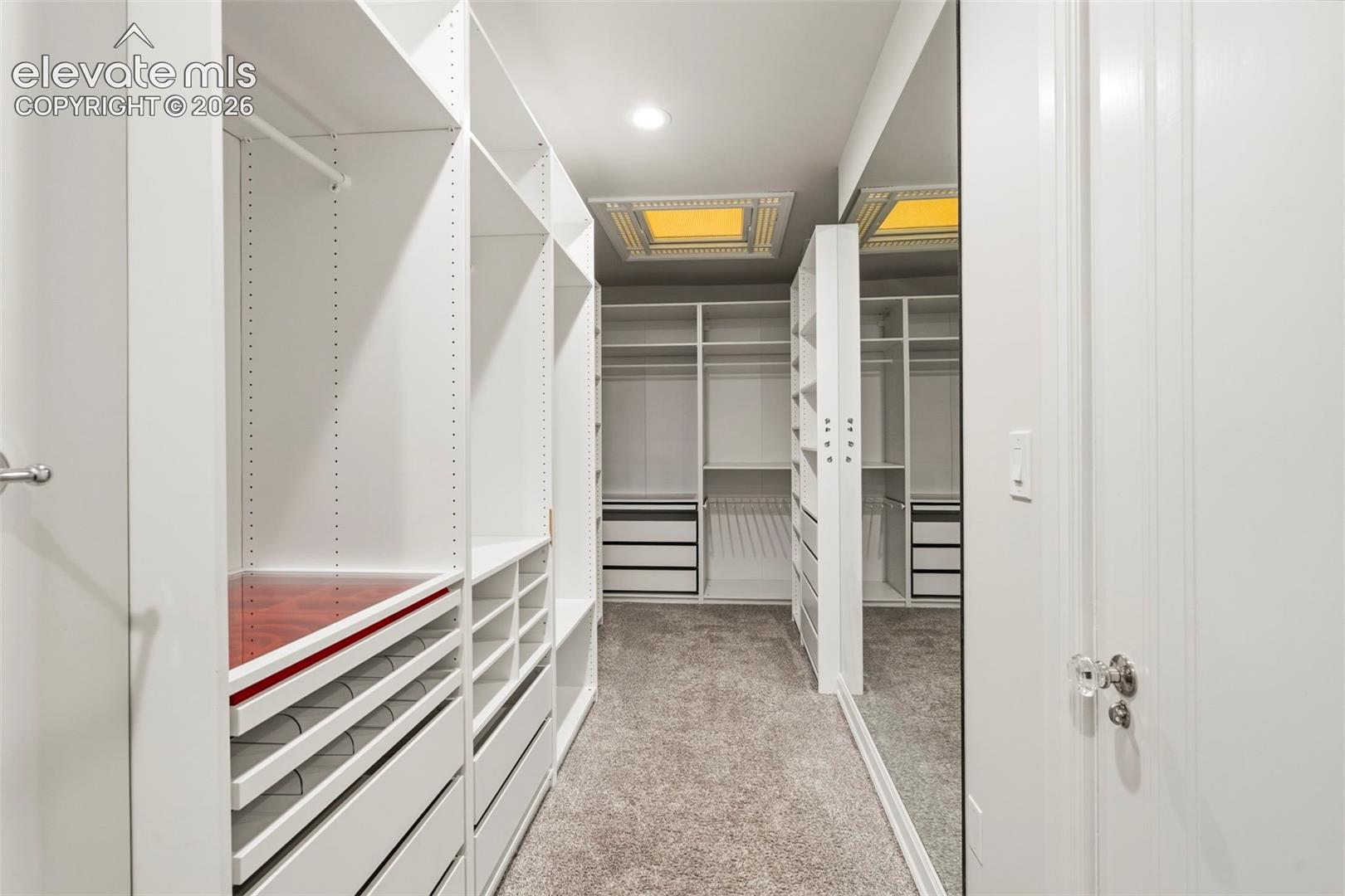 Walk-in closet featuring floor-to-ceiling white built-in shelving, multiple pull-out drawers, full-height wall mirrors, and recessed ceiling lighting