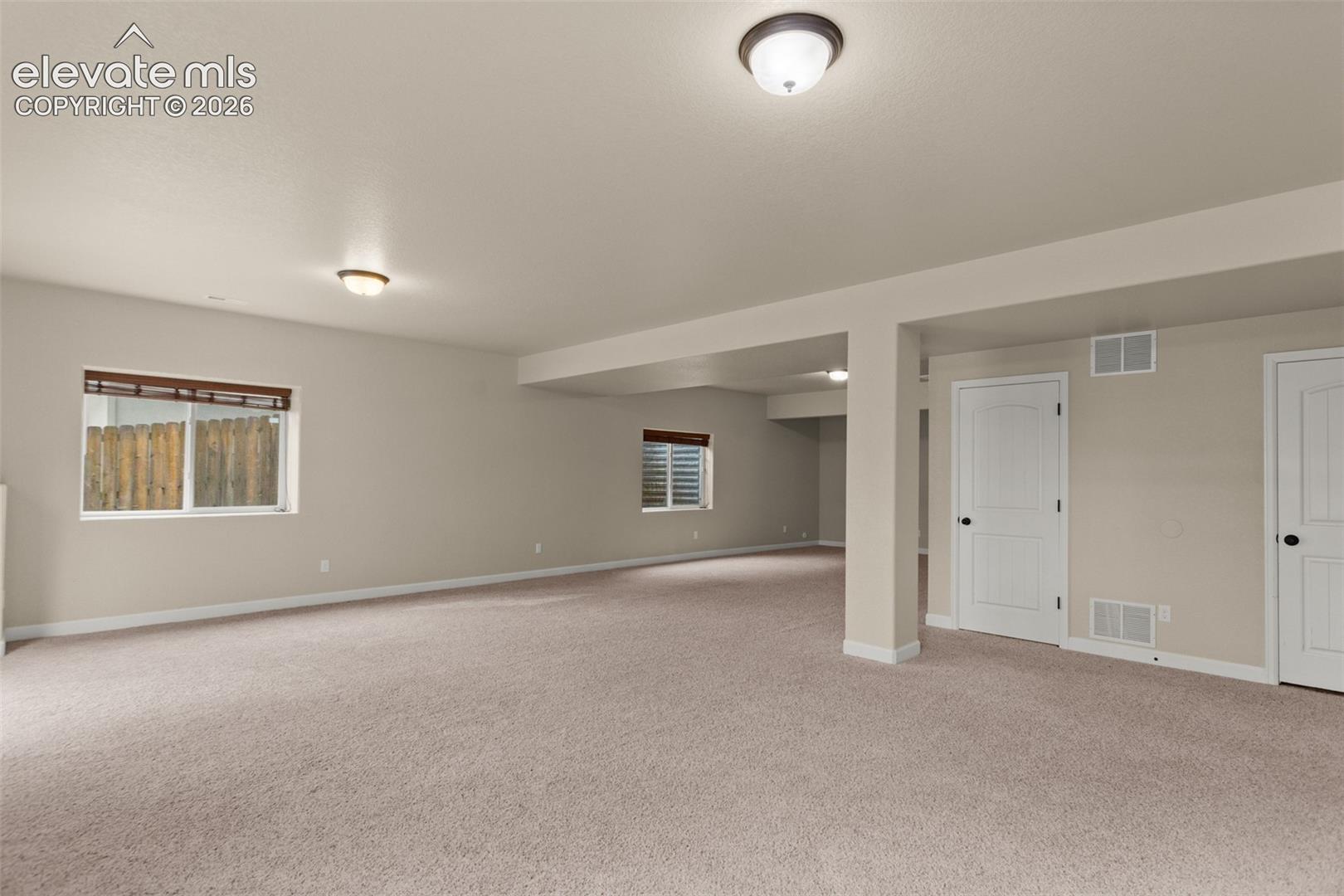 Open-concept interior space featuring wall-to-wall carpeting, neutral wall tones, two slider windows, and two white solid-core interior doors