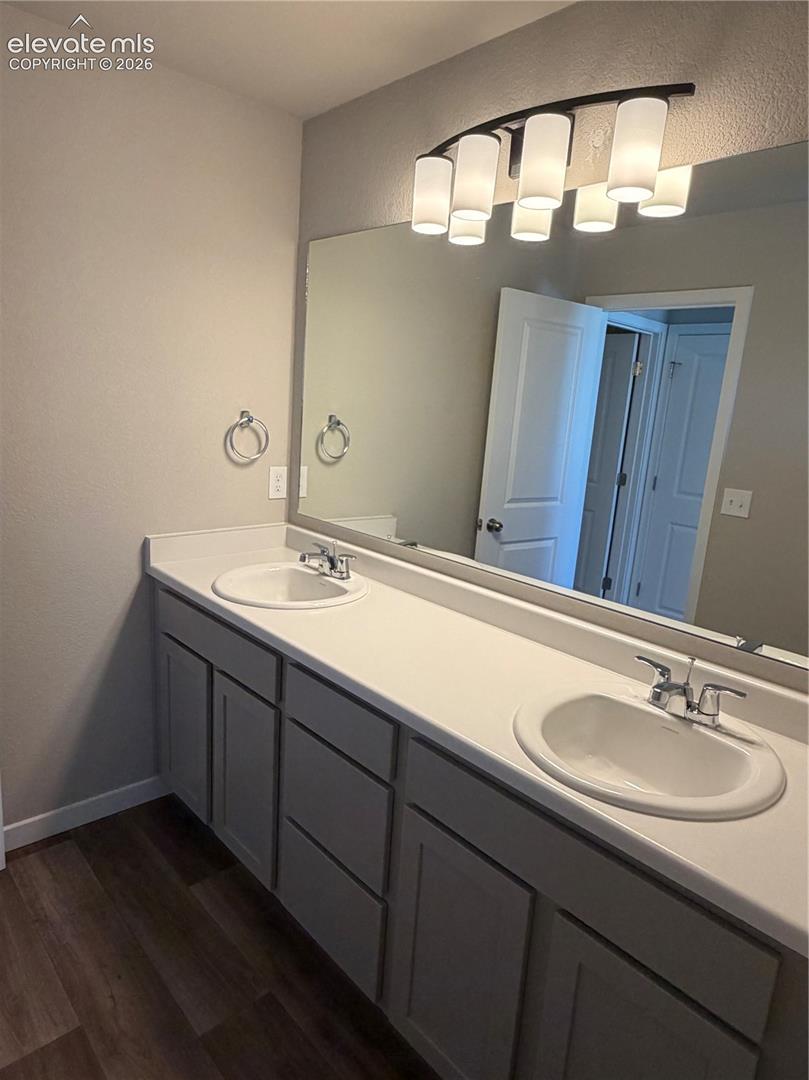 Double vanity featuring a solid surface countertop, dual integrated sinks, gray shaker-style cabinetry, and a full-width wall-mounted mirror