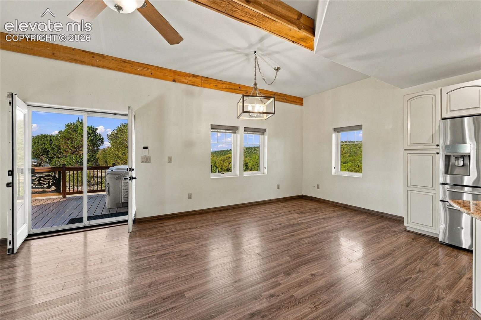 Dining Area with exposed wood beams, wood-finish flooring, stainless steel refrigerator, geometric pendant lighting, and double glass doors opening to an exterior deck