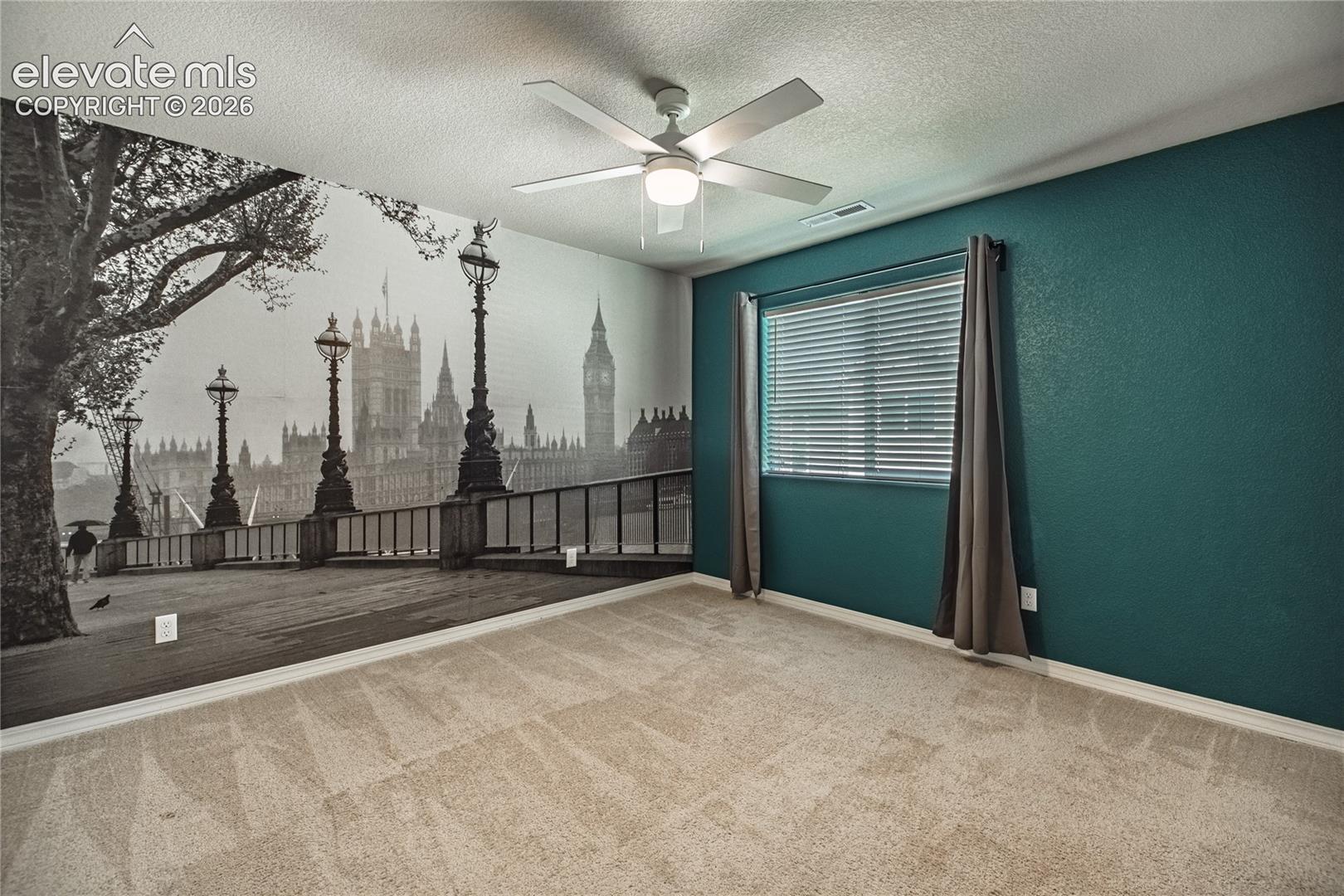 Wall mural accent, deep teal painted walls, neutral carpet, ceiling fan, and window with blinds