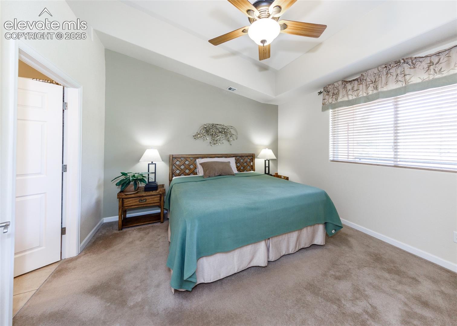 Tray ceiling, neutral wall tones, carpeted flooring, and a ceiling fan with integrated lighting